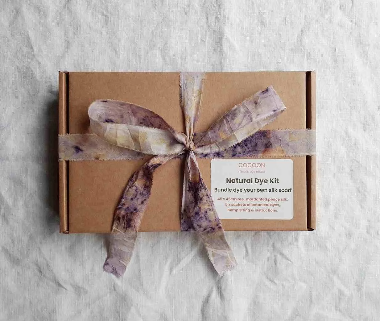 A recycled cardboard gift box wrapped in a bundle dyed silk ribbon