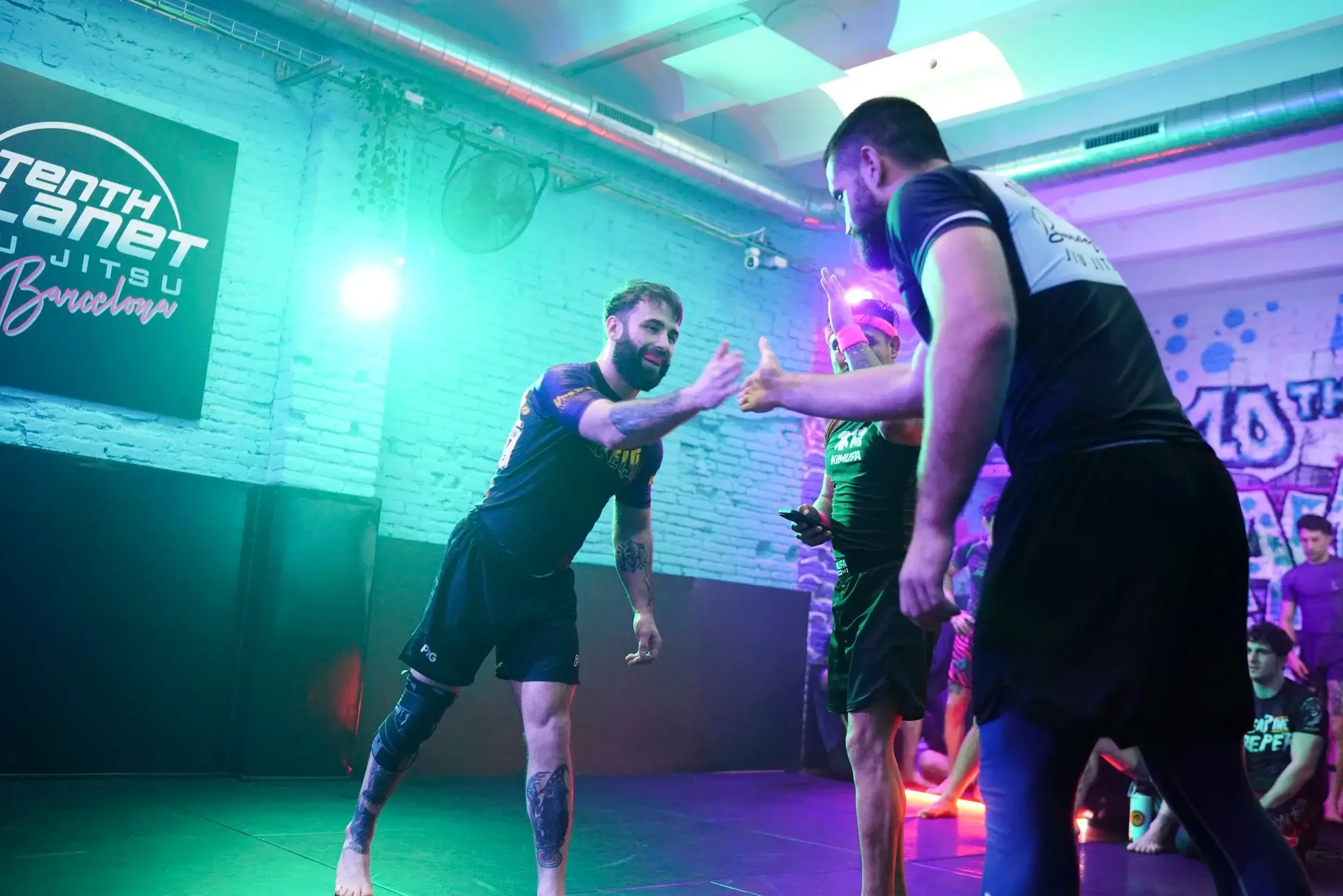 Two men in black shirts and shorts giving each other high five in a gym with neon lights.