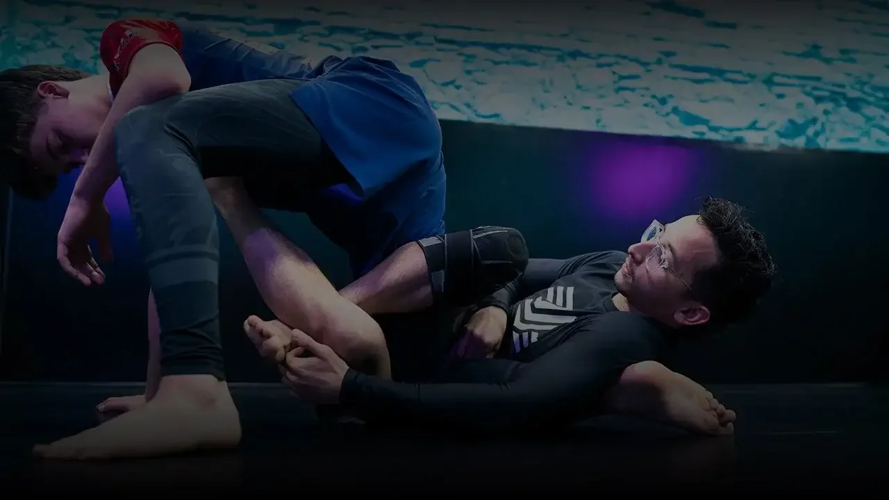 Two men practicing Brazilian Jiu-Jitsu on a mat near a pool; one man is applying a submission hold on the other.