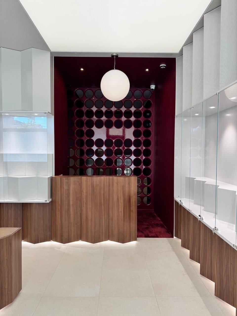 Kabinet Studios developed and manufactured the custom furniture using walnut veneer, burgundy-painted interiors, secure display glass, and high-CRI LED lighting. From technical detailing to final installation