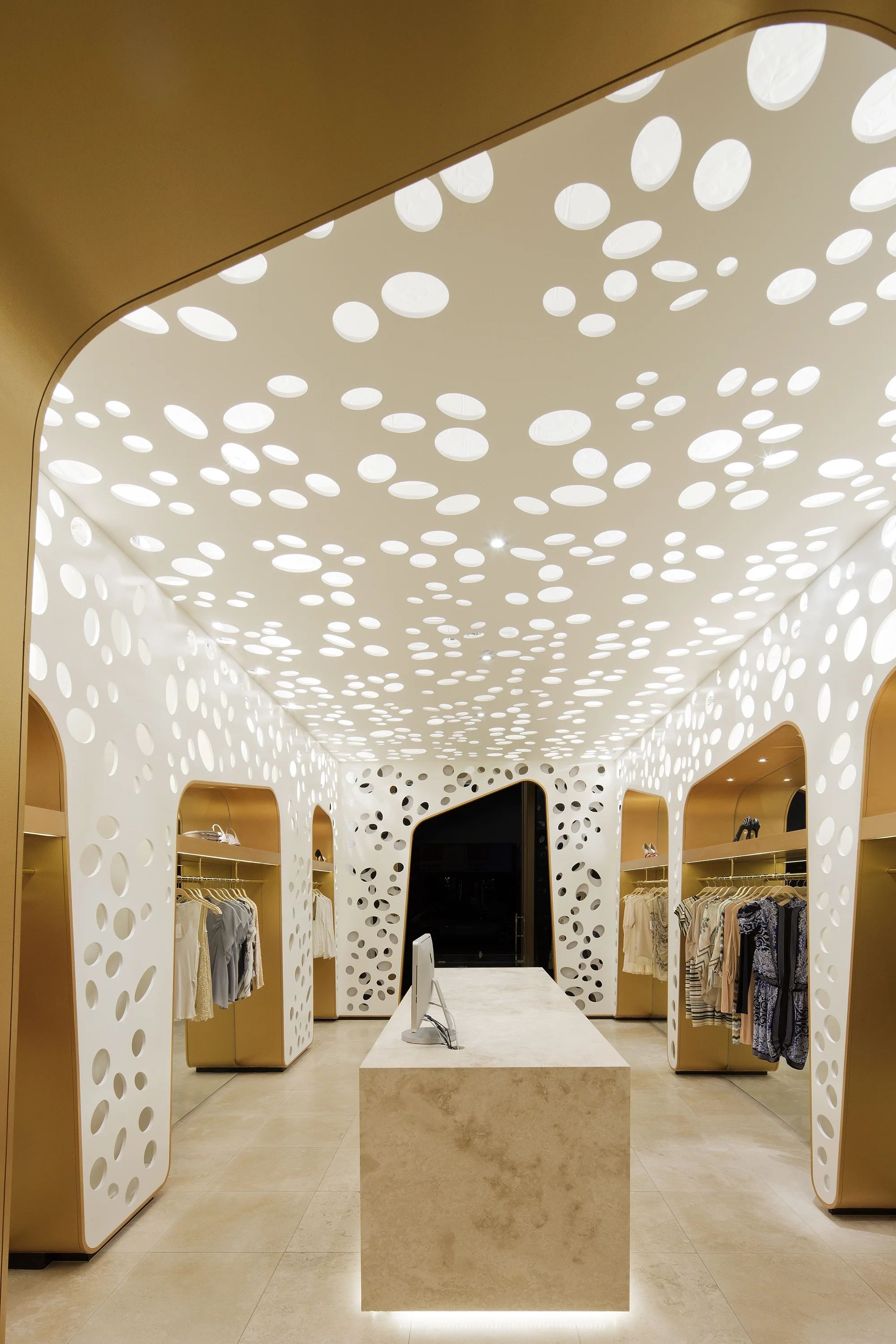 Hinterleuchtete, perforierte, weiße Wände schaffen Spannung in dem kleinen Verkaufsraum für hochwertige Damenmode.