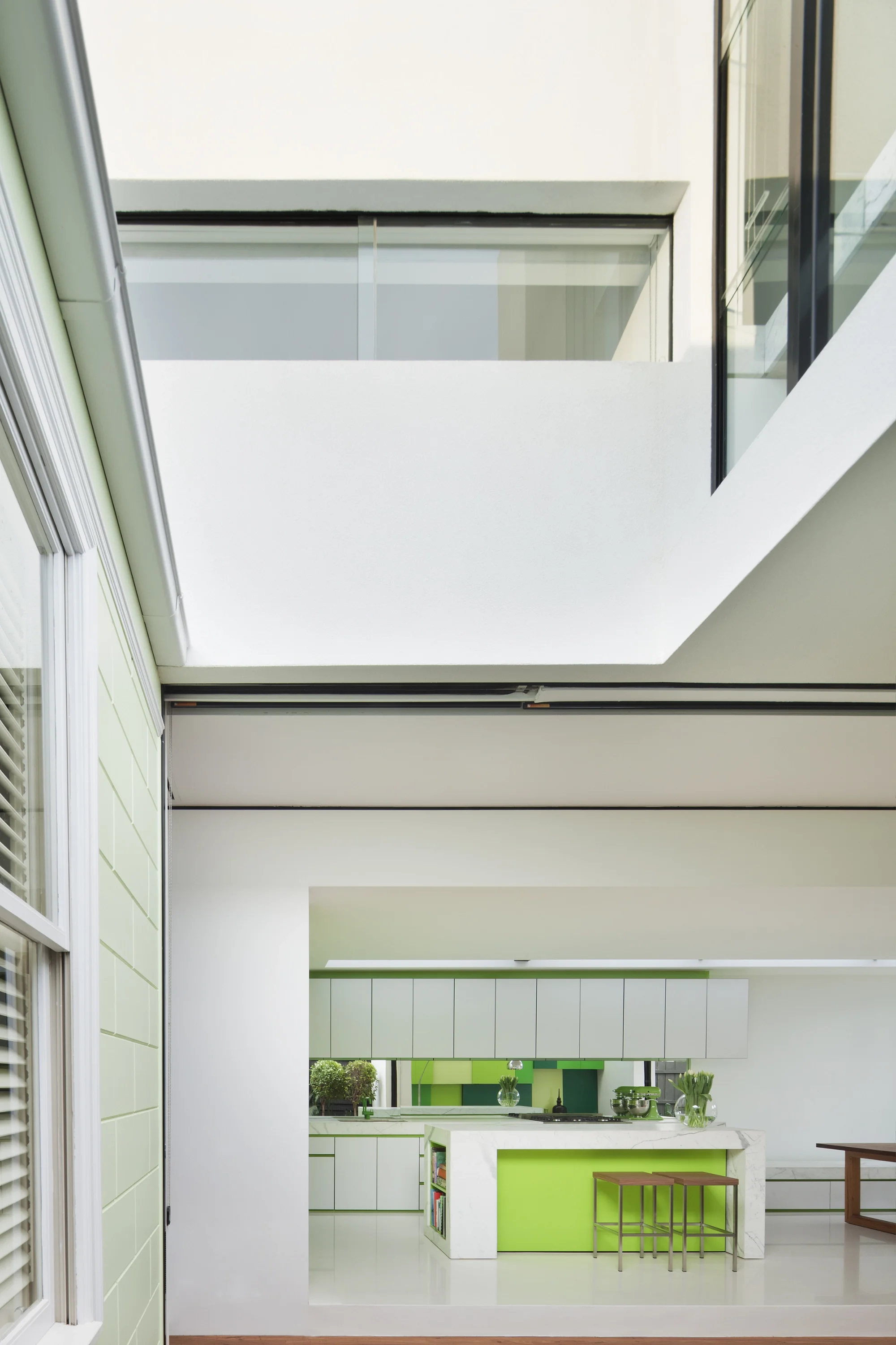 Moderner Anbau an einem denkmalgeschützten Haus, geöffnete Glasfront gibt Blick auf die moderne Küche mit glatten Küchenfronten in weiß und der Akzentfarbe Hellgrün frei.