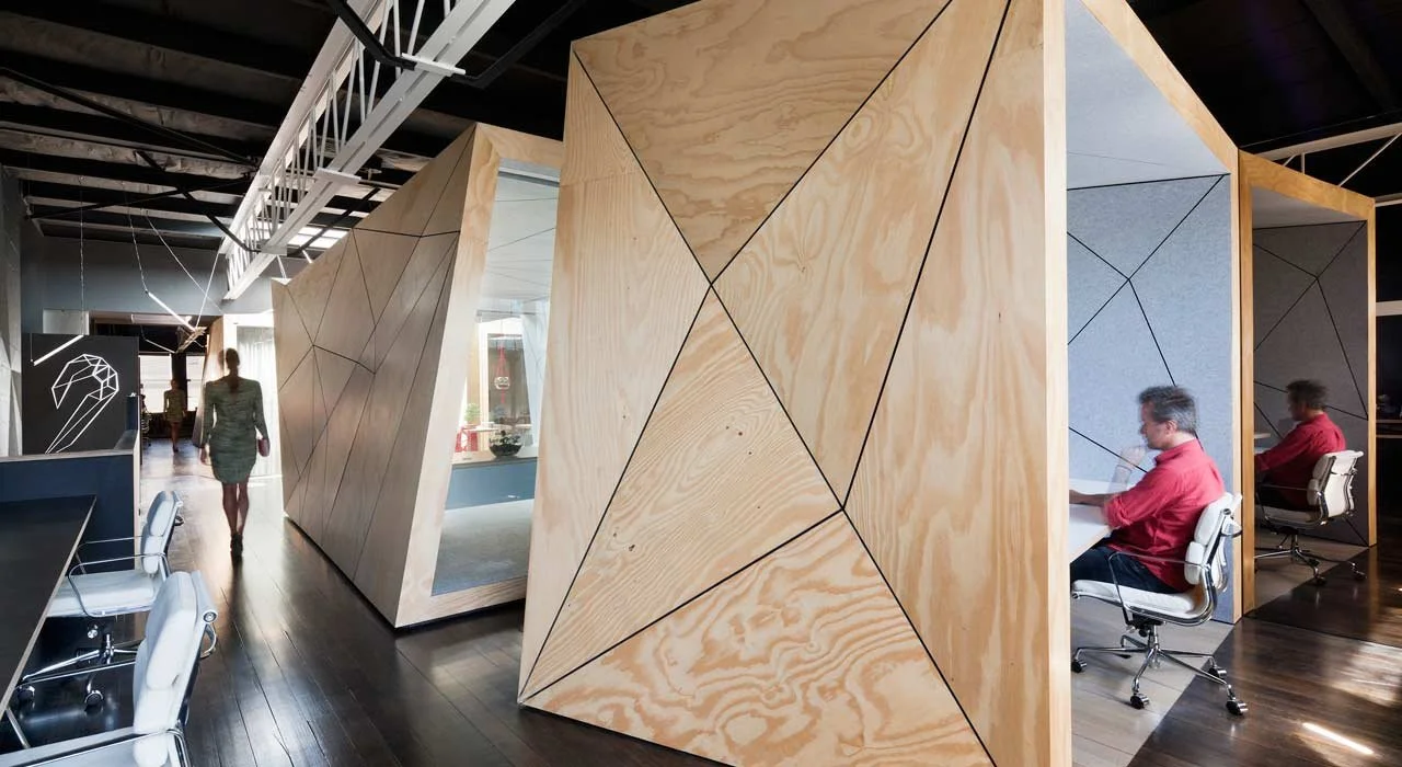 Futuristische Editing Pods aus Holzfacetten mit Innenflächen aus grauem Filz. Schreibtische in schwarz oder weiß mit weißen Lederbürostühlen.