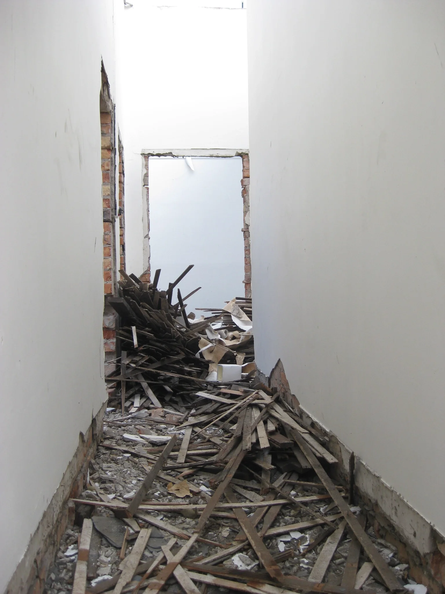 Ein denkmalgeschütztes Gebäude während der Sanierung, mit eingestürztem Dach und herumliegenden Holz- und Bauschutt sowie offenem Durchgang zum nächsten Raum.