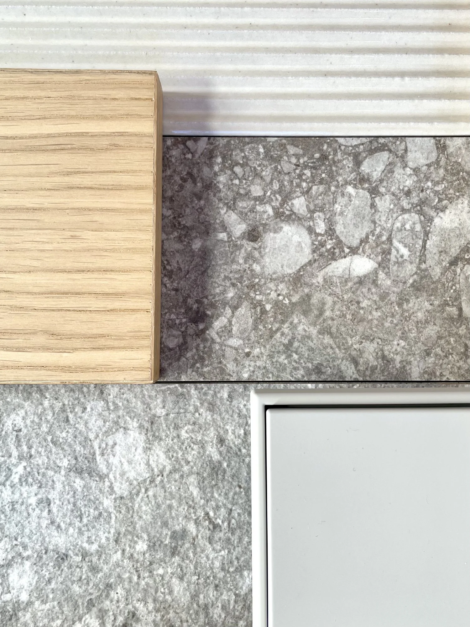 Ein Blick auf verschiedene Oberflächen: Ein Ausschnitt eines Holzstücks mit horizontalen Linien, zwei Steinböden mit unterschiedlichen Strukturen und Farben, und ein moderner Lichtschalter in Aluminium im unteren rechten Bereich.