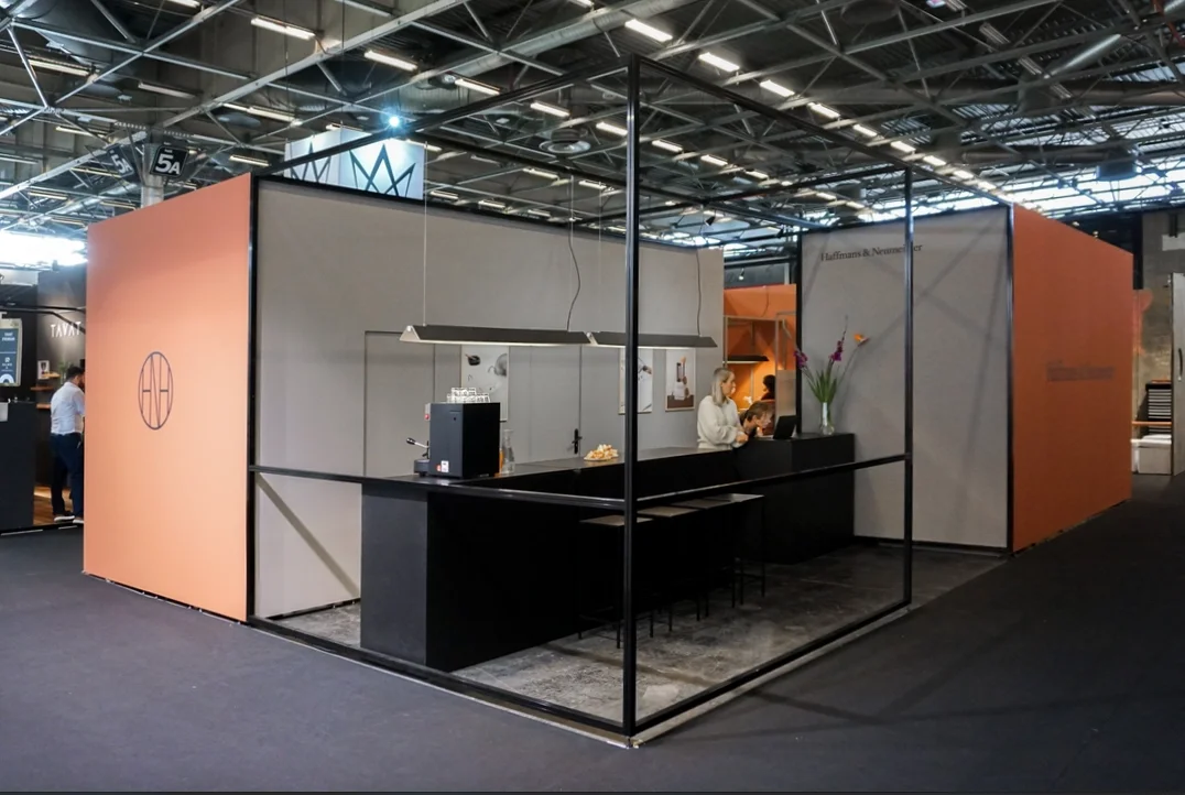 Einladender Empfangsbereich des wiederverwendbaren Messestands mit schwarzen Barmöbeln und Pendelleuchten.