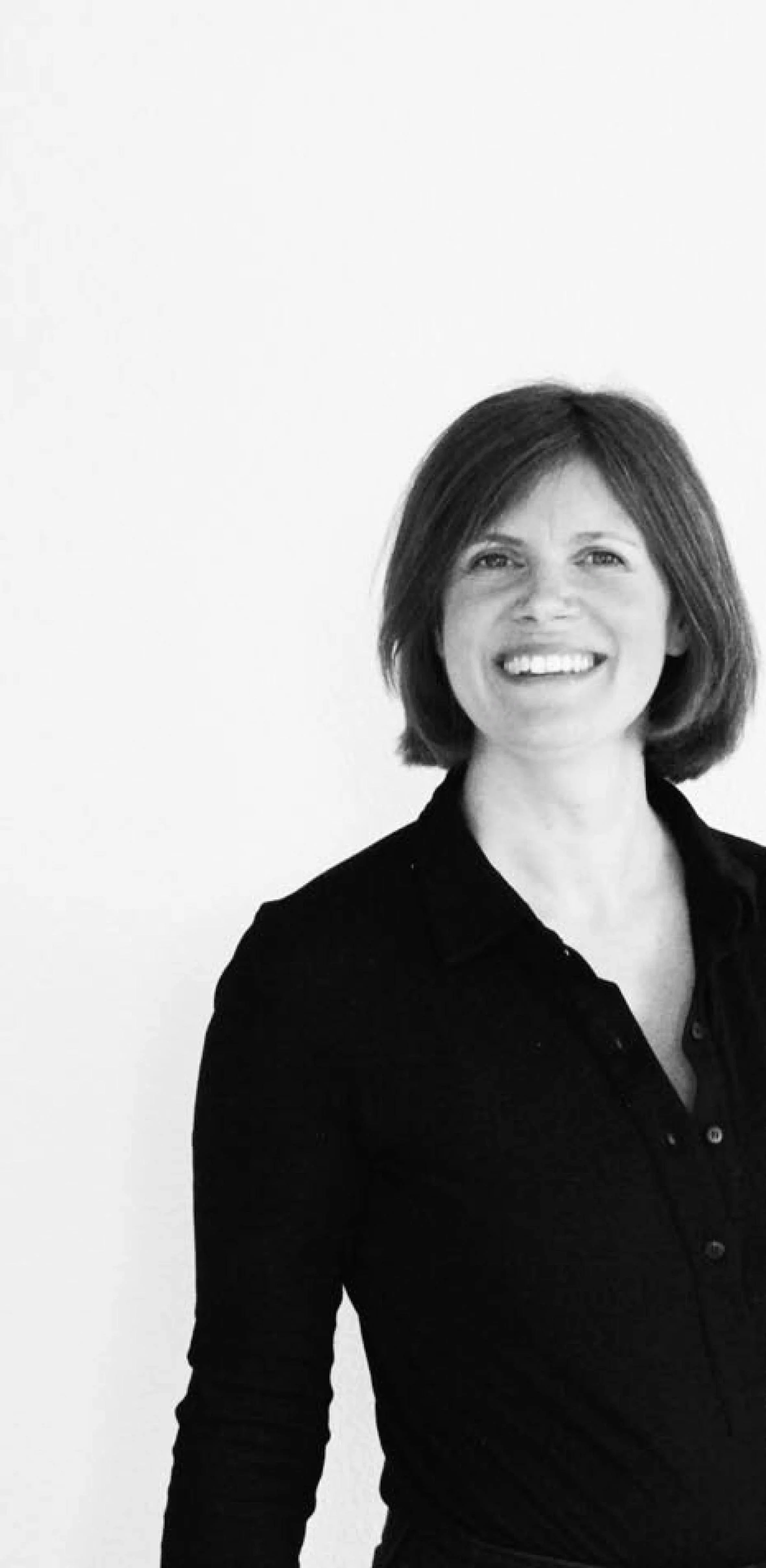 Schwarz-weiß-Porträt einer Innenarchitektin mit schulterlangem Haar, mit einer dunklen Bluse, vor hellem Hintergrund. Gründerin des Designkollektivs Studio Interiors.