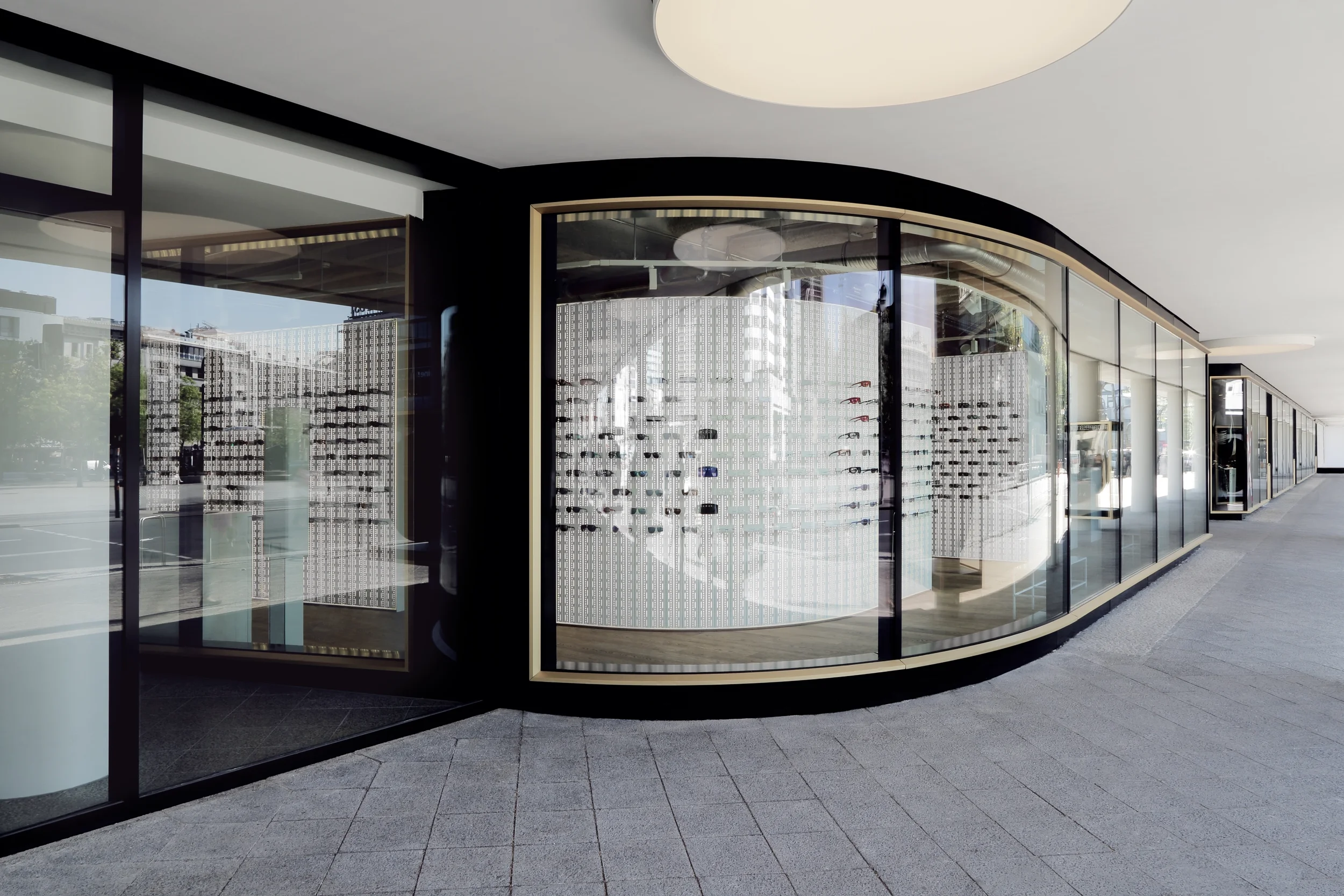 Gerundete Schaufensterfassade in Schwarz und Gold mit Blick auf einen Shop mit weißer Präsentationswand, die der Kurve der Fassade folgt.