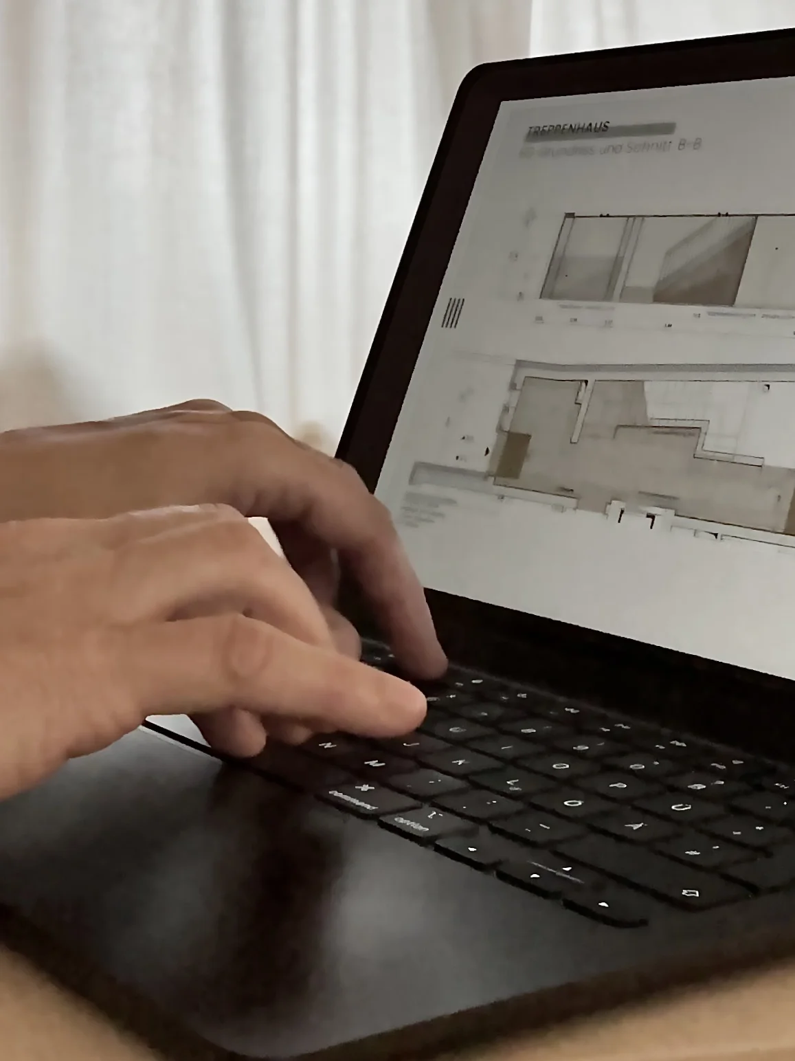 Nahaufnahme von Händen, die an einem Laptop arbeiten, der einen Grundrissplan auf dem Bildschirm zeigt.