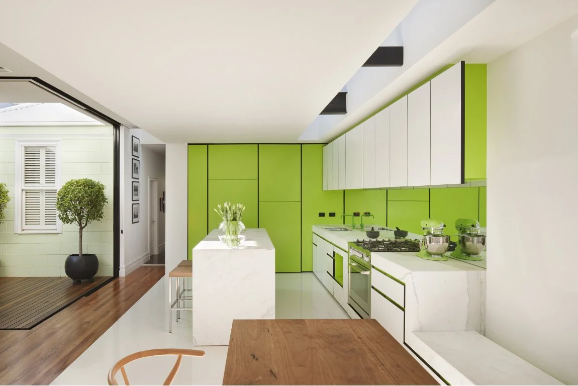 Moderne Küche mit weißen und hellgrünen Fronten, darüber ein Skylight für natürlichen Lichteinfall. Große Glasschiebetüren sind vollständig geöffnet und verbinden den begrünten Innenhof mit der Küche.