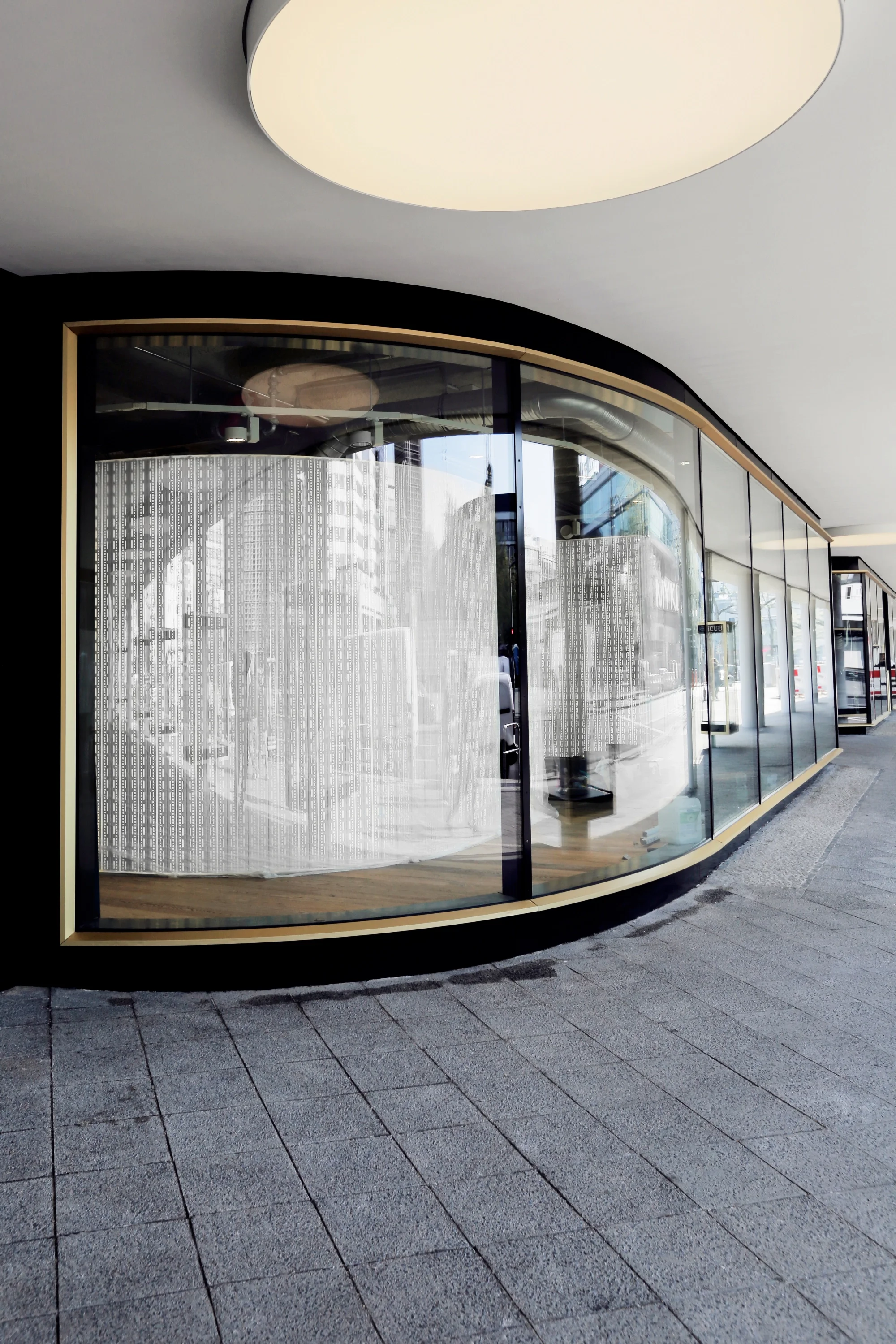 Gerundete Schaufensterfassade gibt den Blick auf die ebenso gerundete Produktpräsentationswand im Inneren des Stores frei.