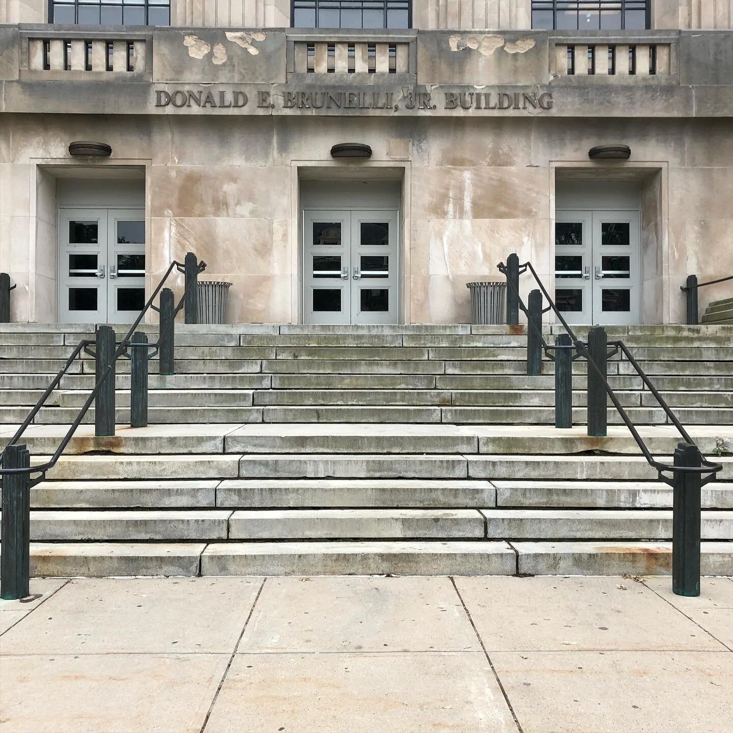 Steps leading to the entrance of a government building with "Donald E. Brunelli, Jr. Building" inscribed above the doors.