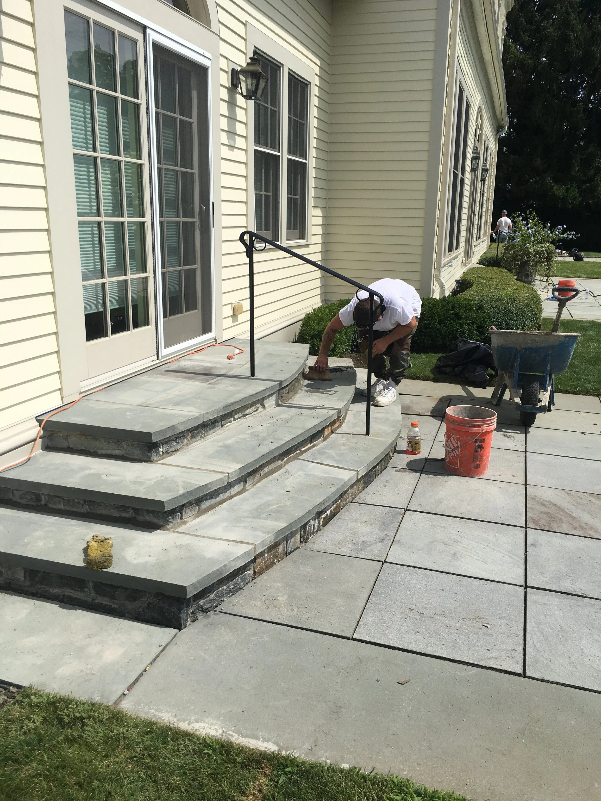 Person working on stone patio steps, using tools near railing.