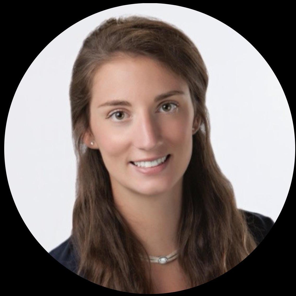 Headshot of a young woman with brown hair, wearing a black top, white necklace, and small earrings, smiling against a white background.