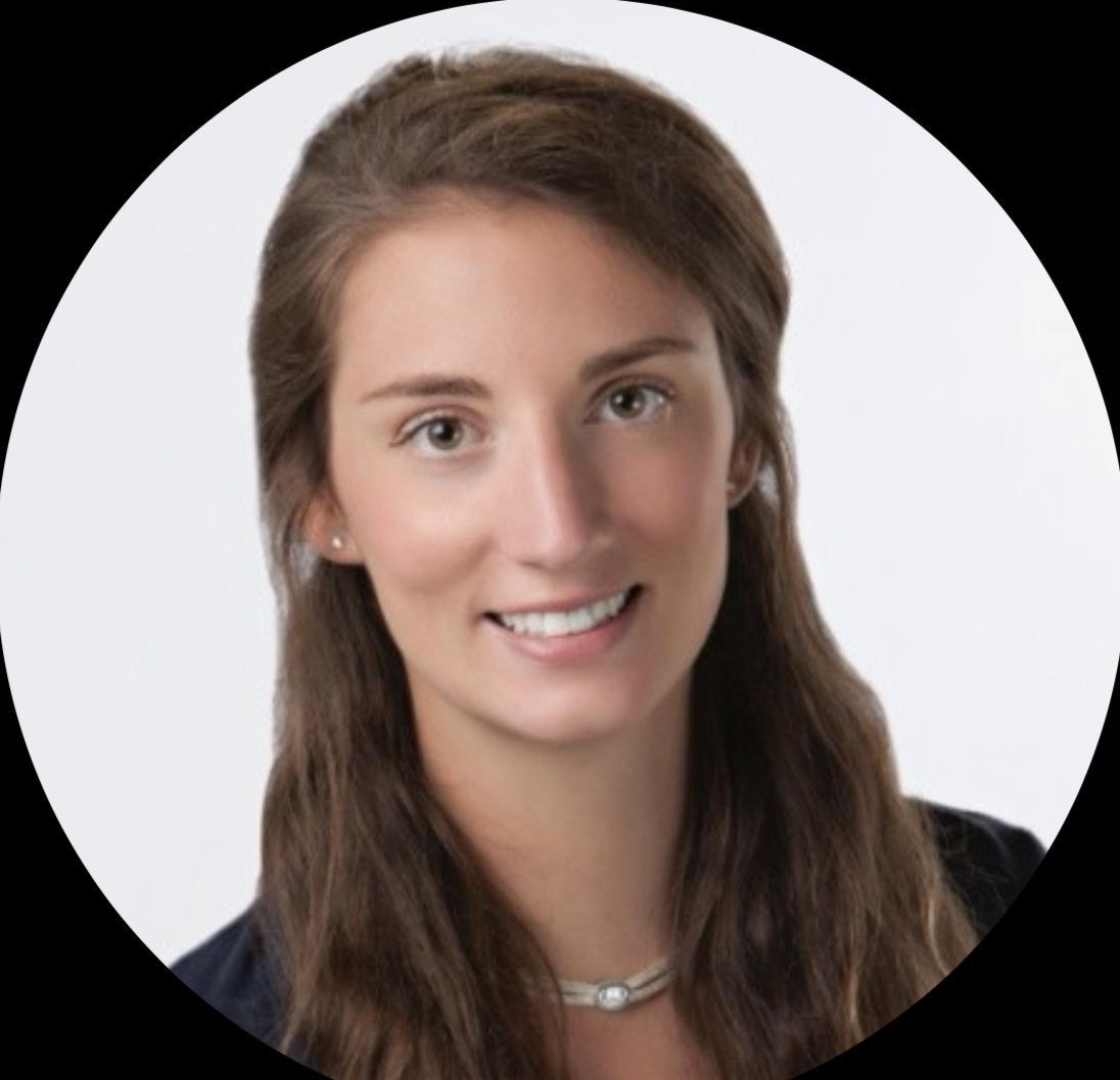 Headshot of a young woman with long brown hair, smiling, wearing a dark top and a necklace, against a plain white background.