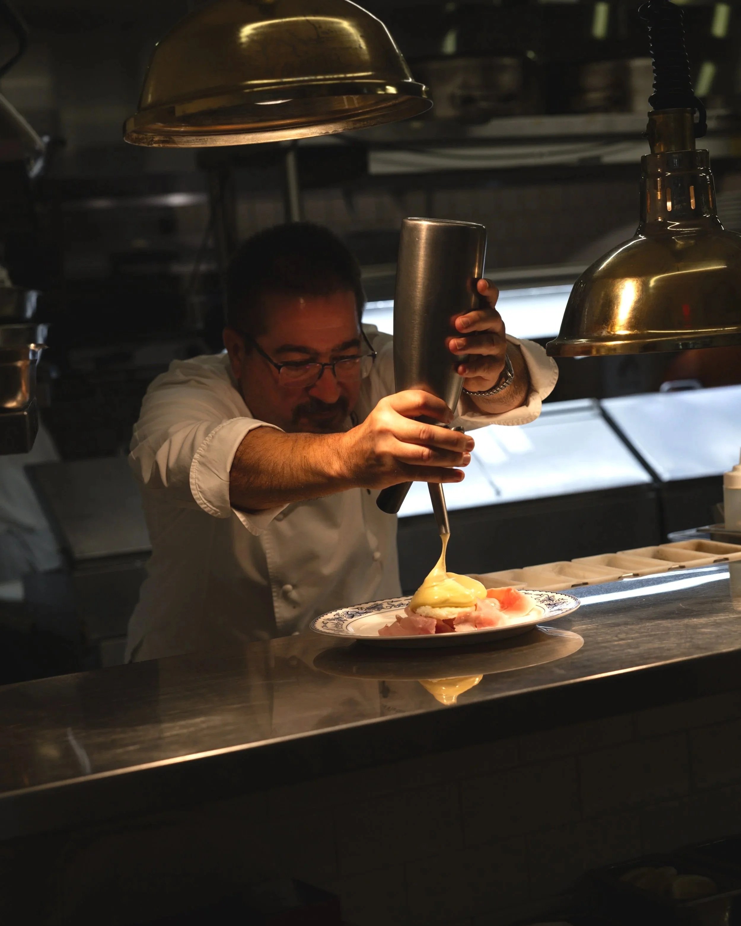 Chef Gianni finishing a plated dish in Bianca’s open kitchen in Culver City under warm kitchen lighting.