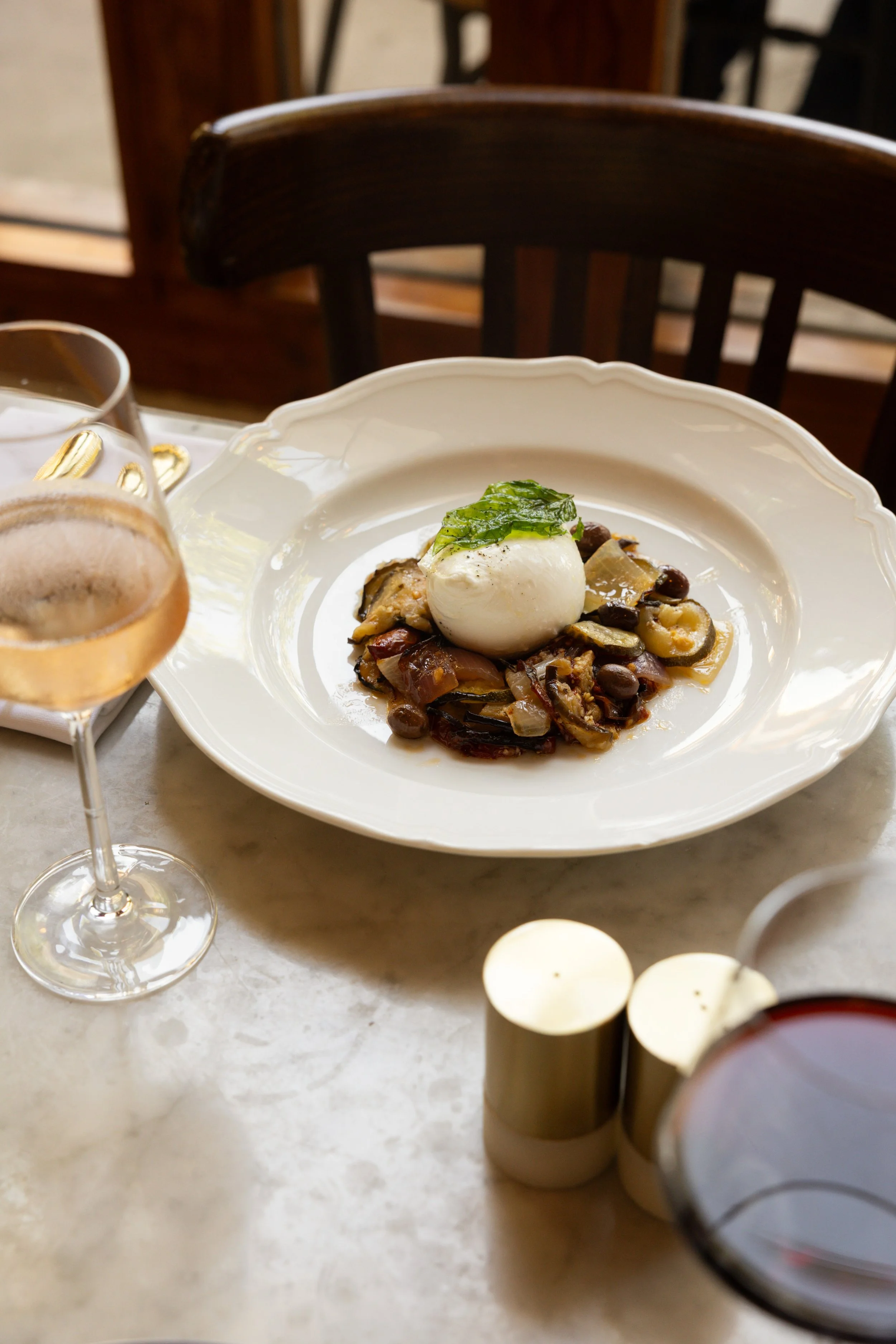 Seasonal plated dish served at Bianca restaurant in Culver City, set on a marble table with wine glasses.