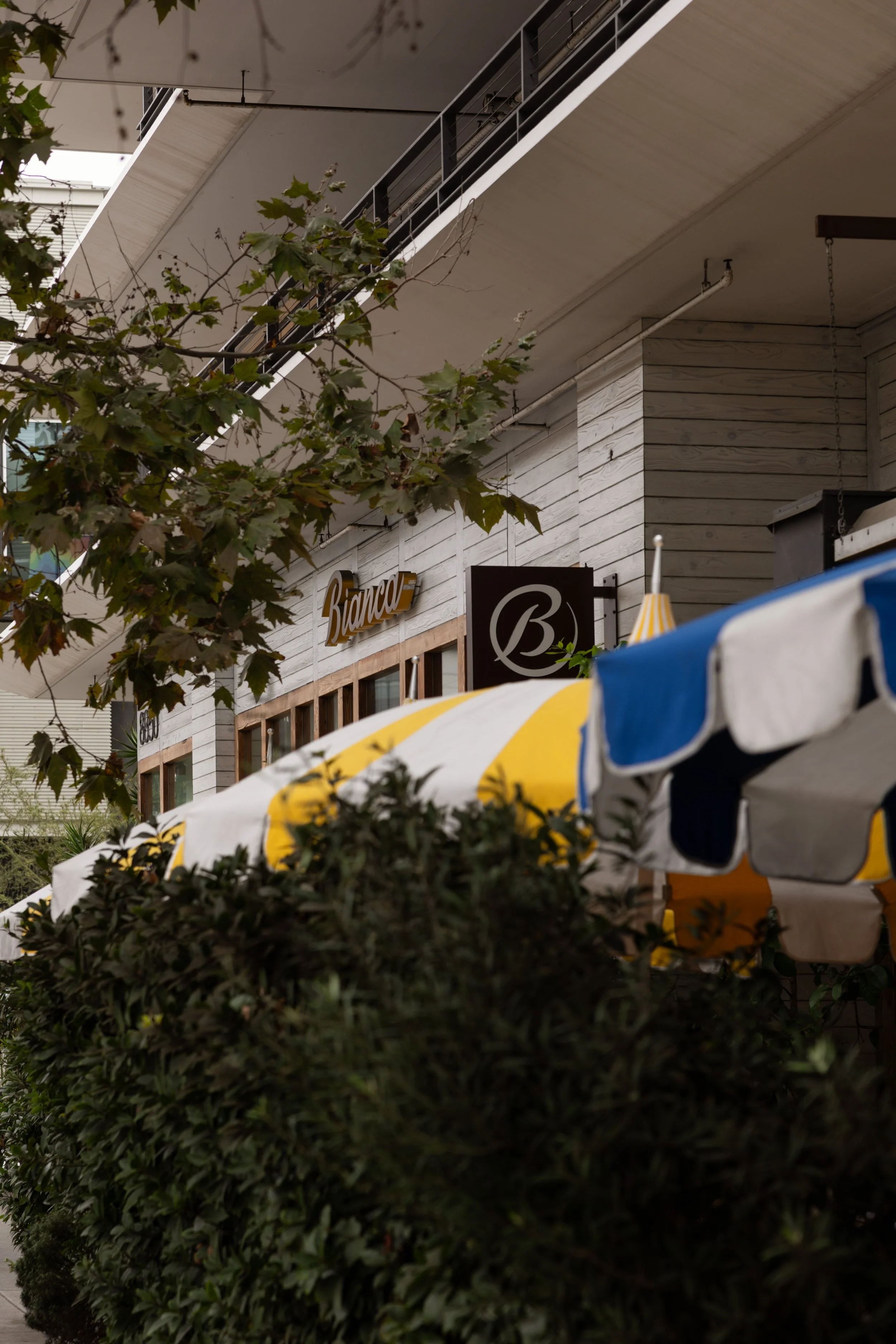 Exterior of Bianca restaurant and bakery in Culver City with striped awnings and surrounding greenery.