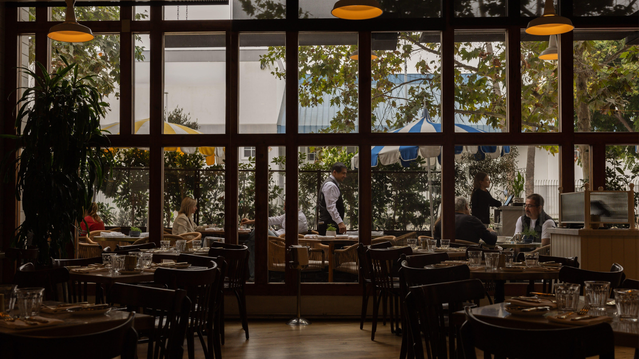 A view from the inside Bianca restuarant looking out at the patio where there are people sitting and a server walking by