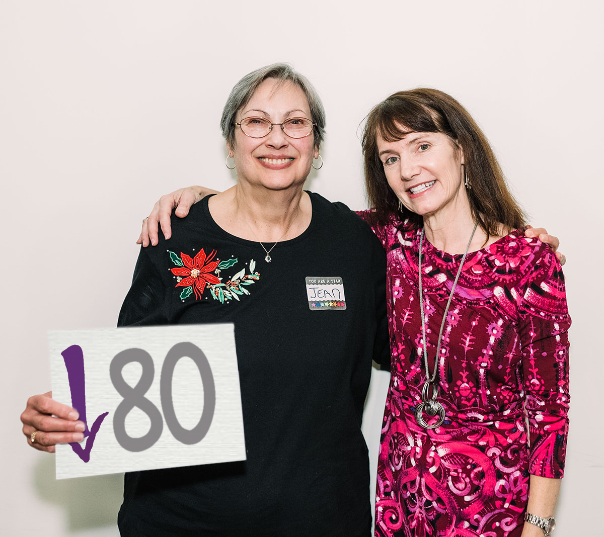 Jean and Coach Gayle stand with their arms around each other's shoulders. Jean is holding a sign that says 80 pounds down. Coach Gayle can help you lose weight and feel great.