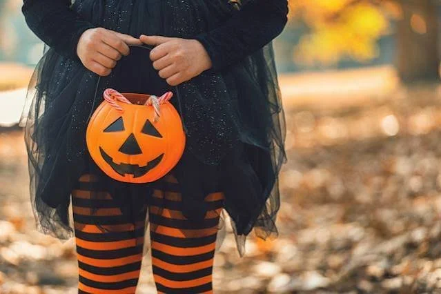 chile dressed for halloween holding a small plastic pumpking with candy