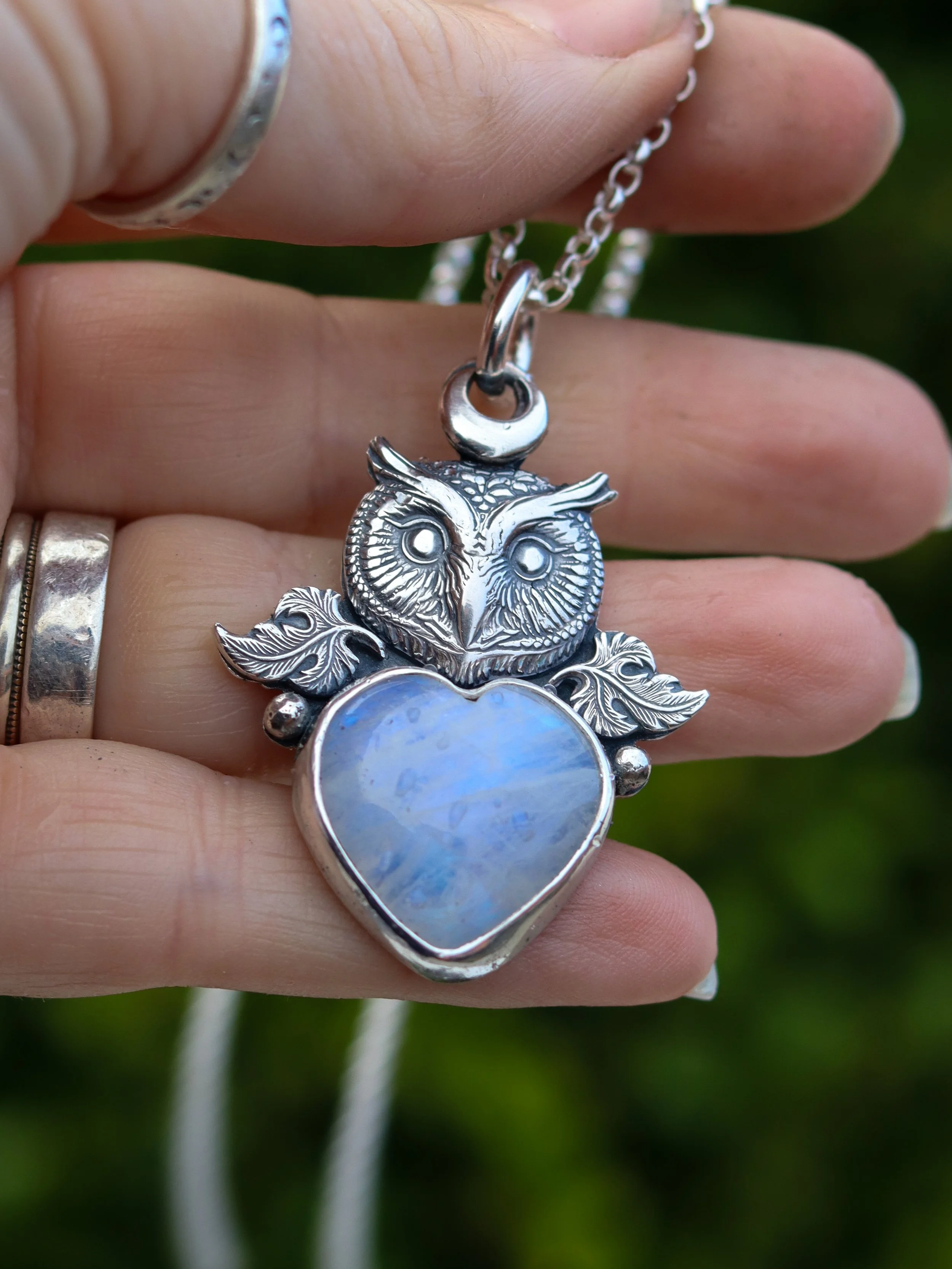 A beautiful owl head cast in sterling silver with leaves and a large moonstone heart. displayed on a storyteller chain, displayed on a hand. by Gemheaven Jewellery