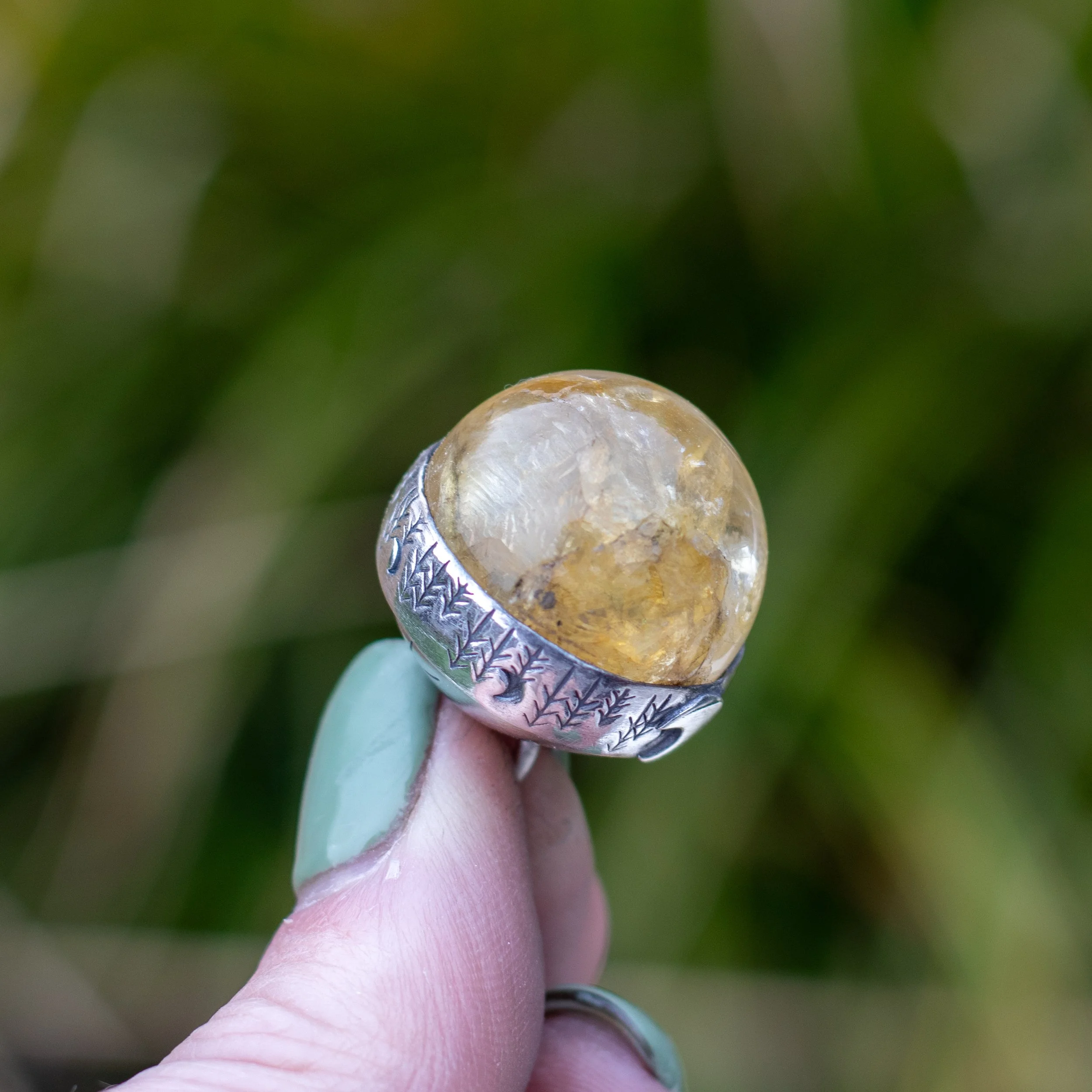 a crystal ball pendant featuring a golden healer sphere encased in a silver band with a natural stamp of foliage and moons