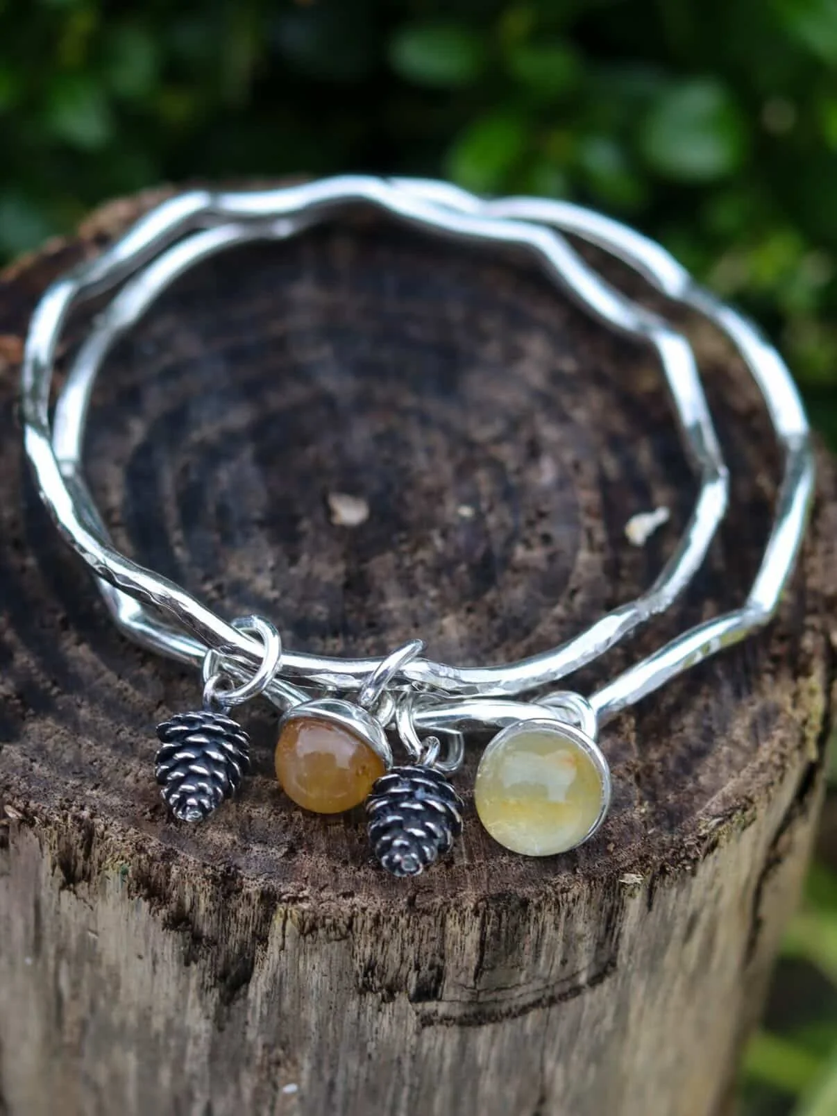 two silver bangles with a silver acorn charm and a golden healer quartz sphere