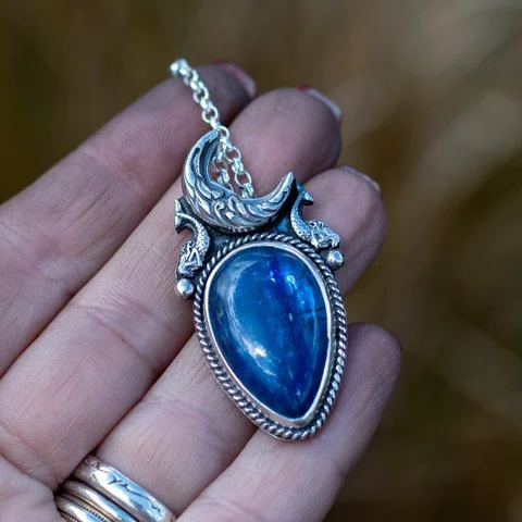 A beautiful denim blue Kyanite with a detailed crescent moon and tiny mermaids decorating the piece.  The back is detailed with stars and waves.