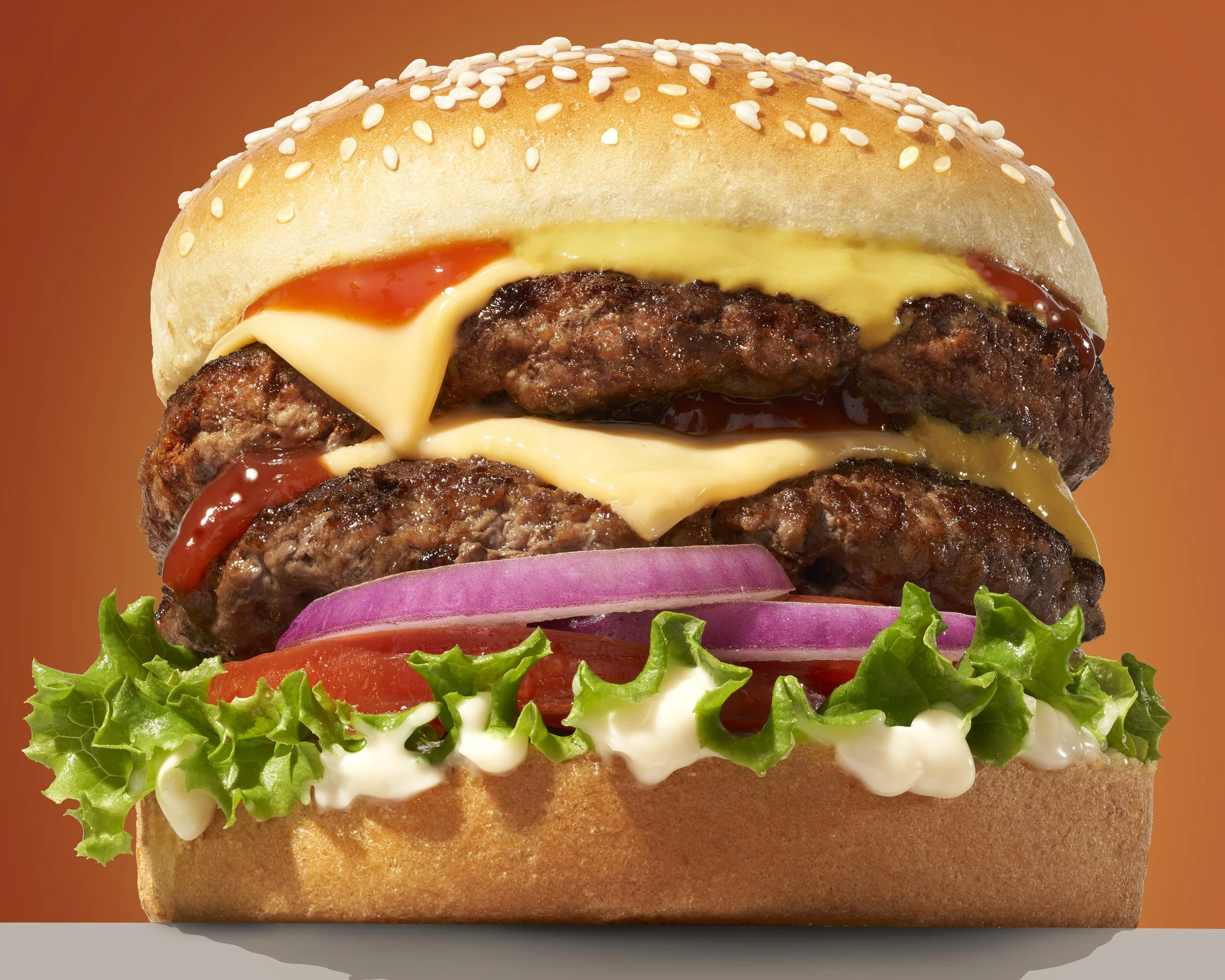 a closeup heroic shot of a double cheeseburger with ketchup, mustard, mayo, lettuce, onion and tomato. 