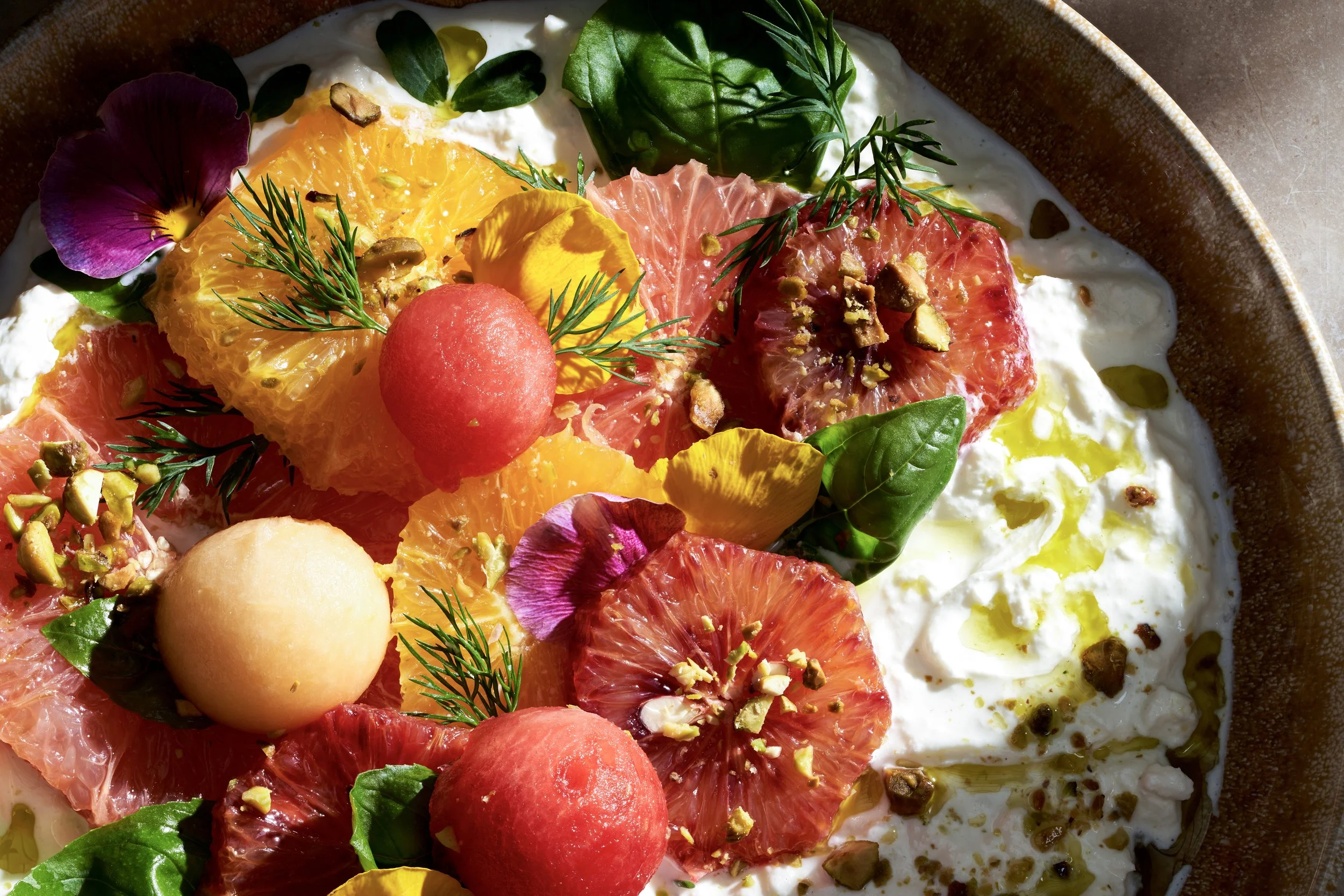 a closeup of a bowl of fresh citrus salad with burrata fresh herbs and buts