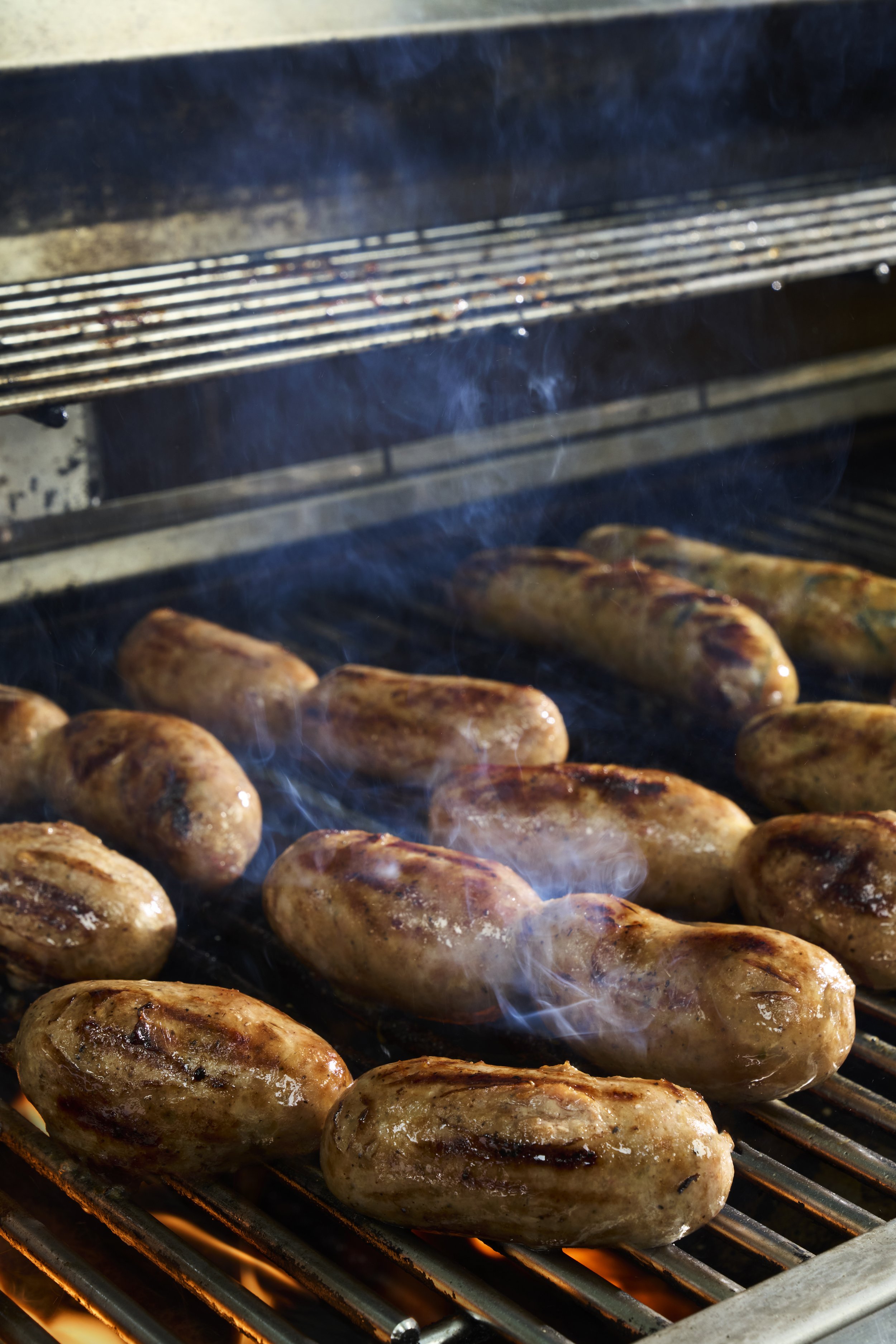 Sausages cooking on a grill with smoke rising.