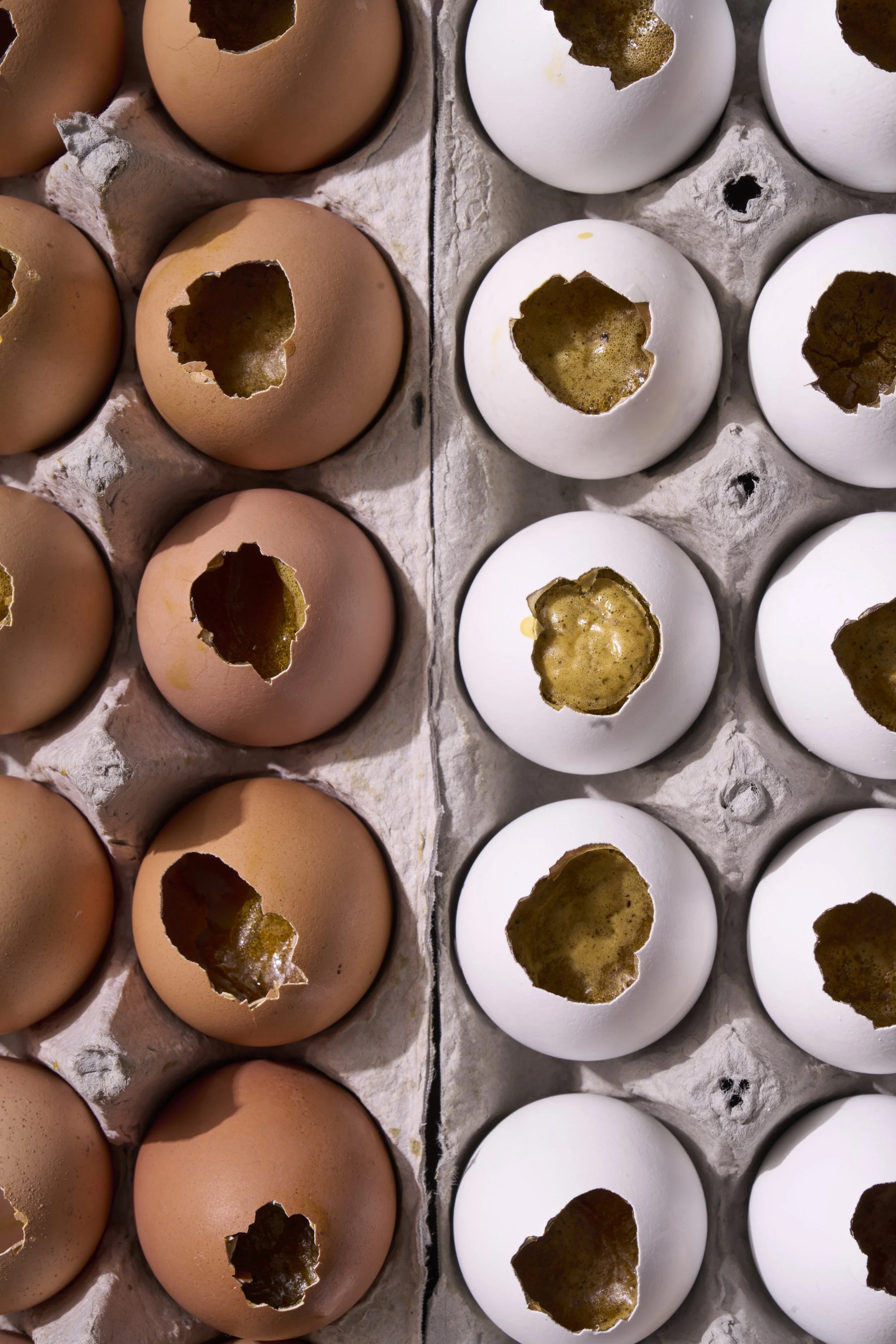 Brown and white eggs with holes burned into their shells, placed in a grey egg carton.