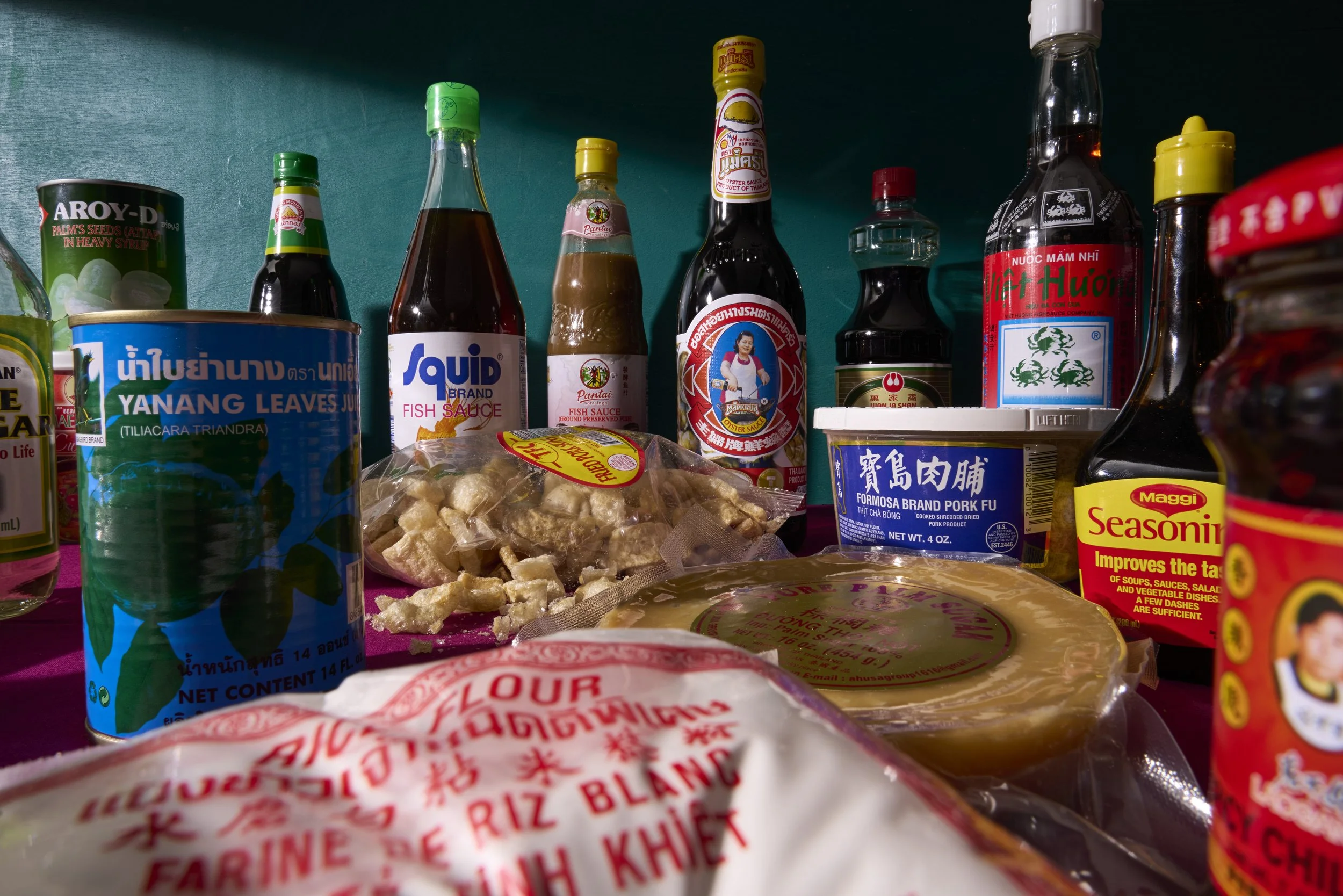 Assorted Asian condiments, canned goods, sauces, and packaged ingredients on a kitchen shelf, including fish sauce, oyster sauce, seasoning, canned vegetables, and dried pork furikake.