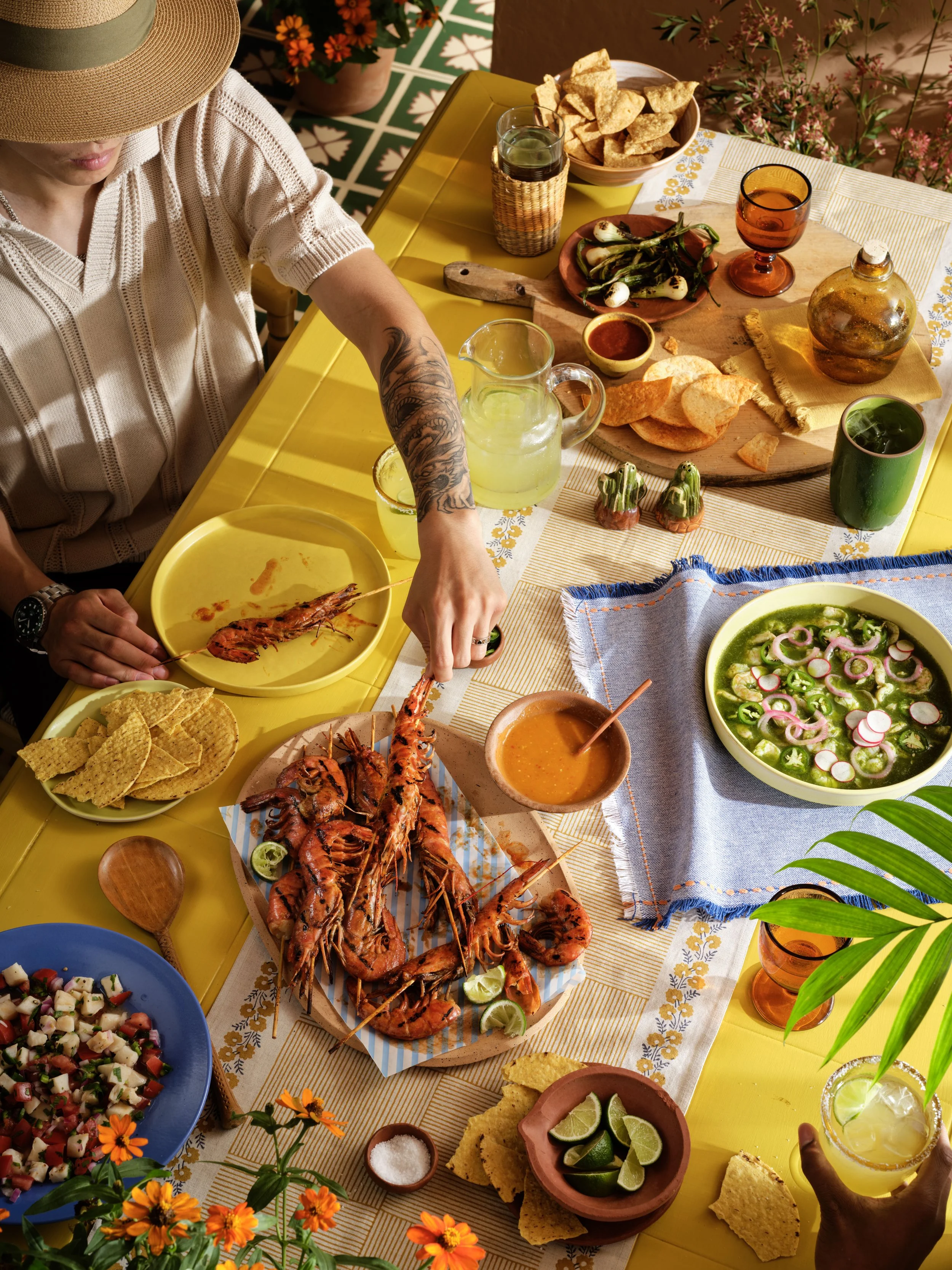 Man sitting at a table full of mexican food, grabbing a shrimp. Warm directional sunlight
