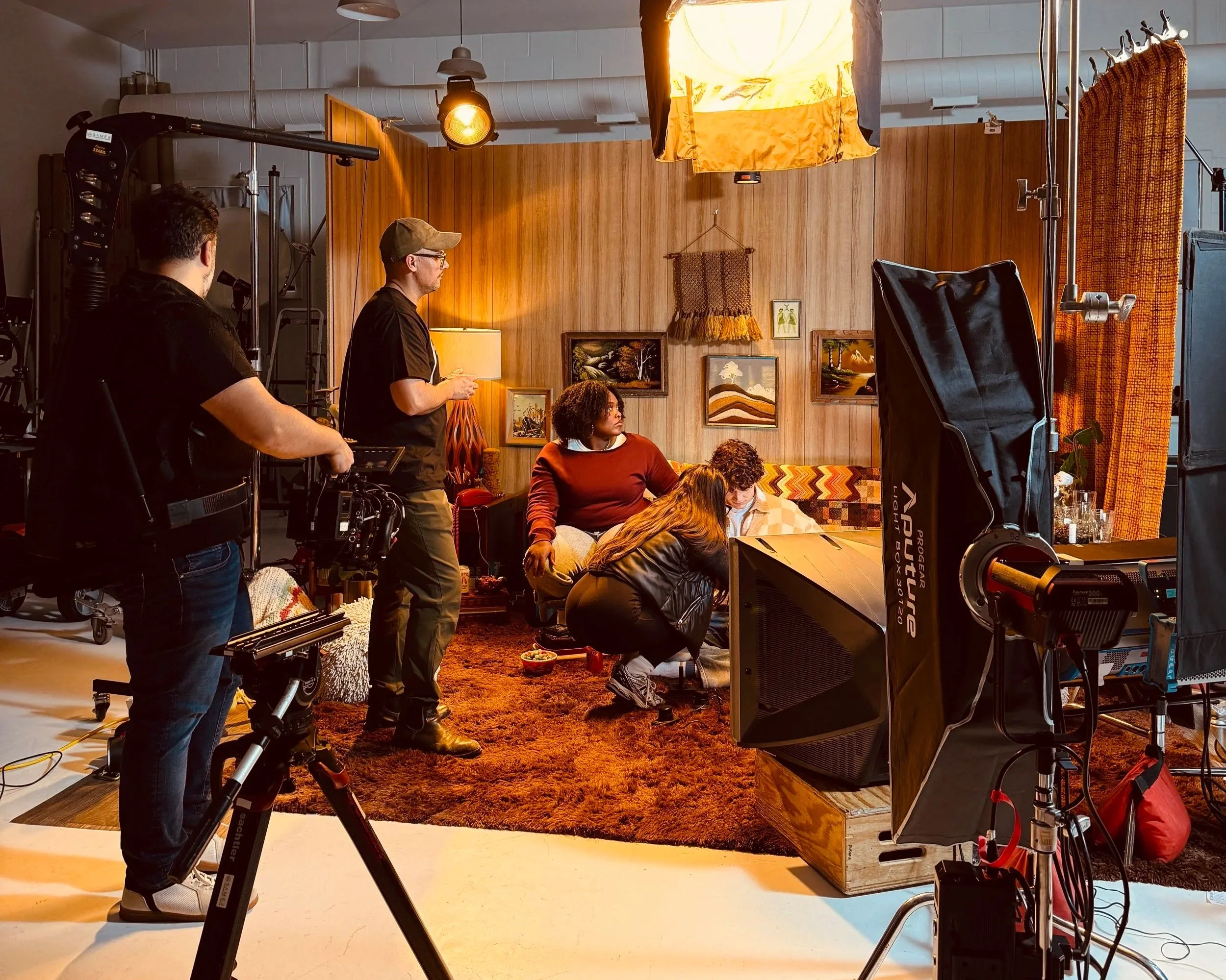 A tv set in a studio with actors, camera crew, director and dp with lighting around the set.