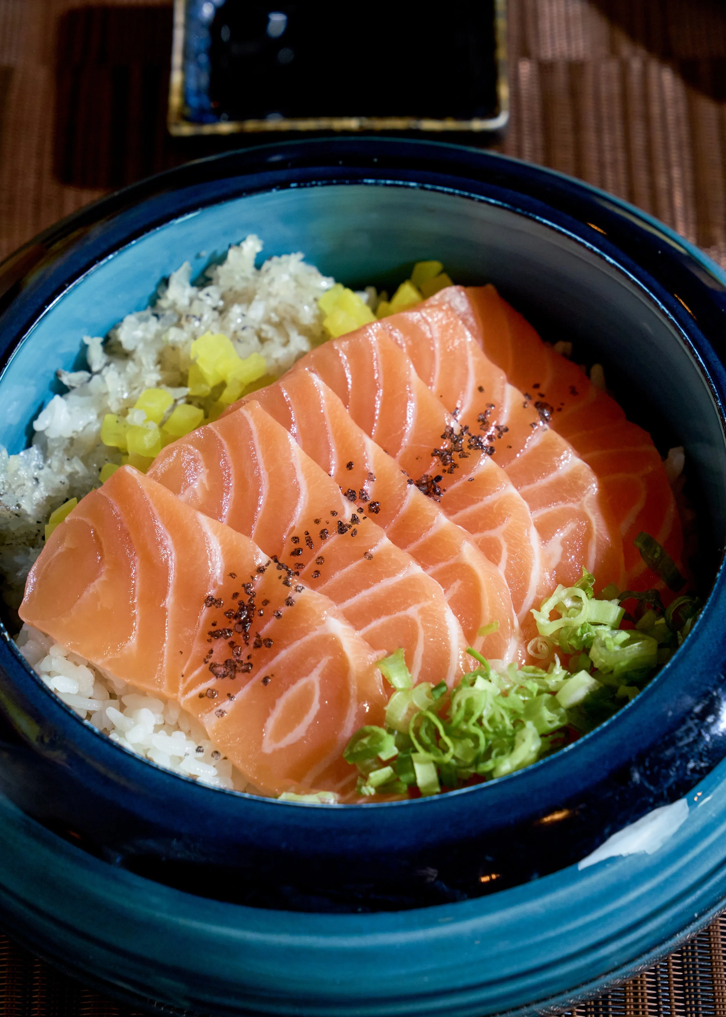 Sashimi bowl with sliced salmon, rice, chopped green onions, wasabi, and a sprinkle of black pepper.