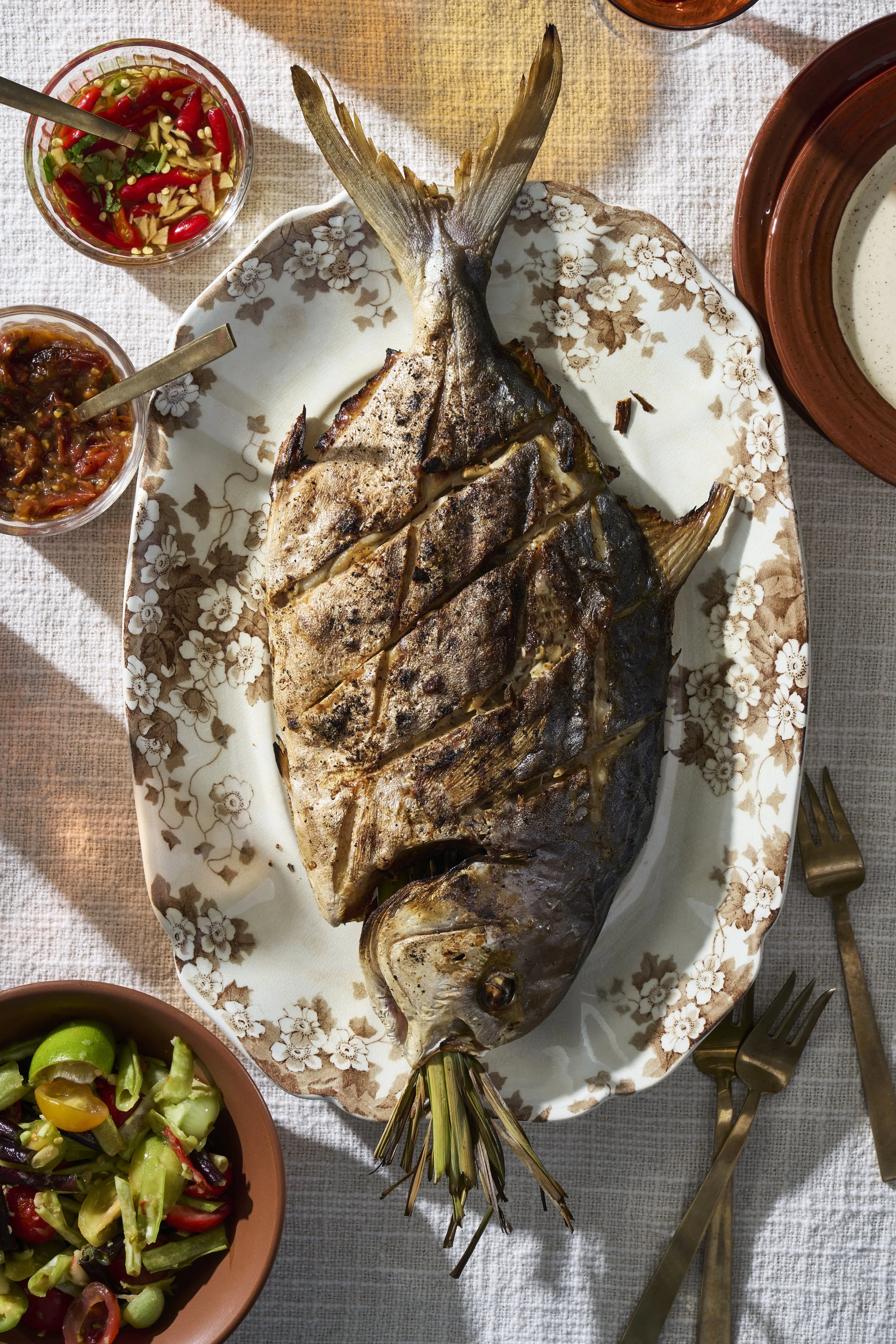 a platter of a fried fish surrounded by drinks and salsas.