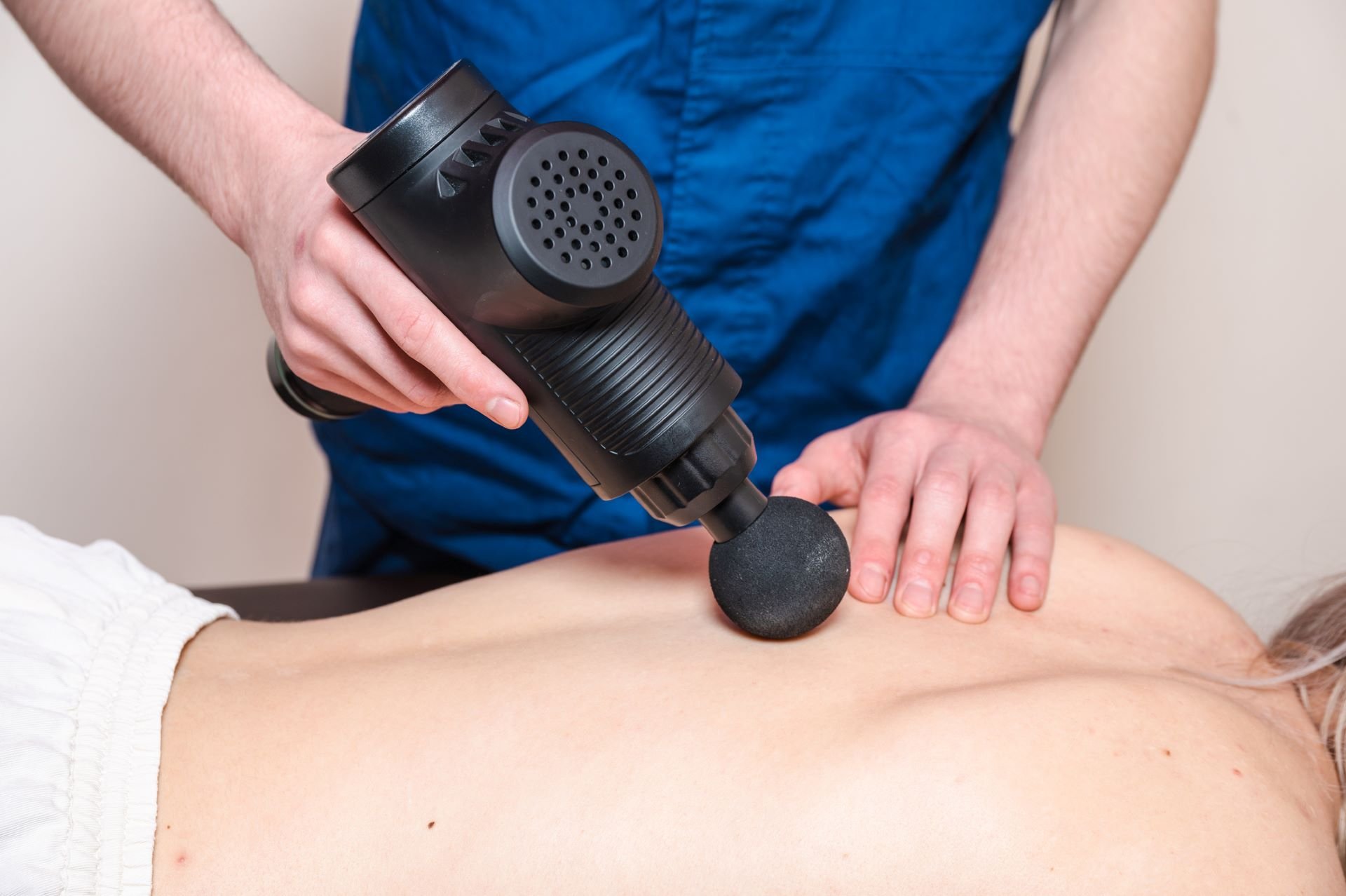 Massage Gun Benefits: What You Need To Know - Masseur+massages+a+girl+with+a+percussion+massager