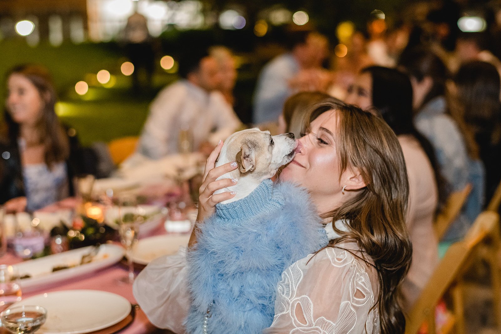 Woman holding and kissing a small dog at a table during a celebration or gathering