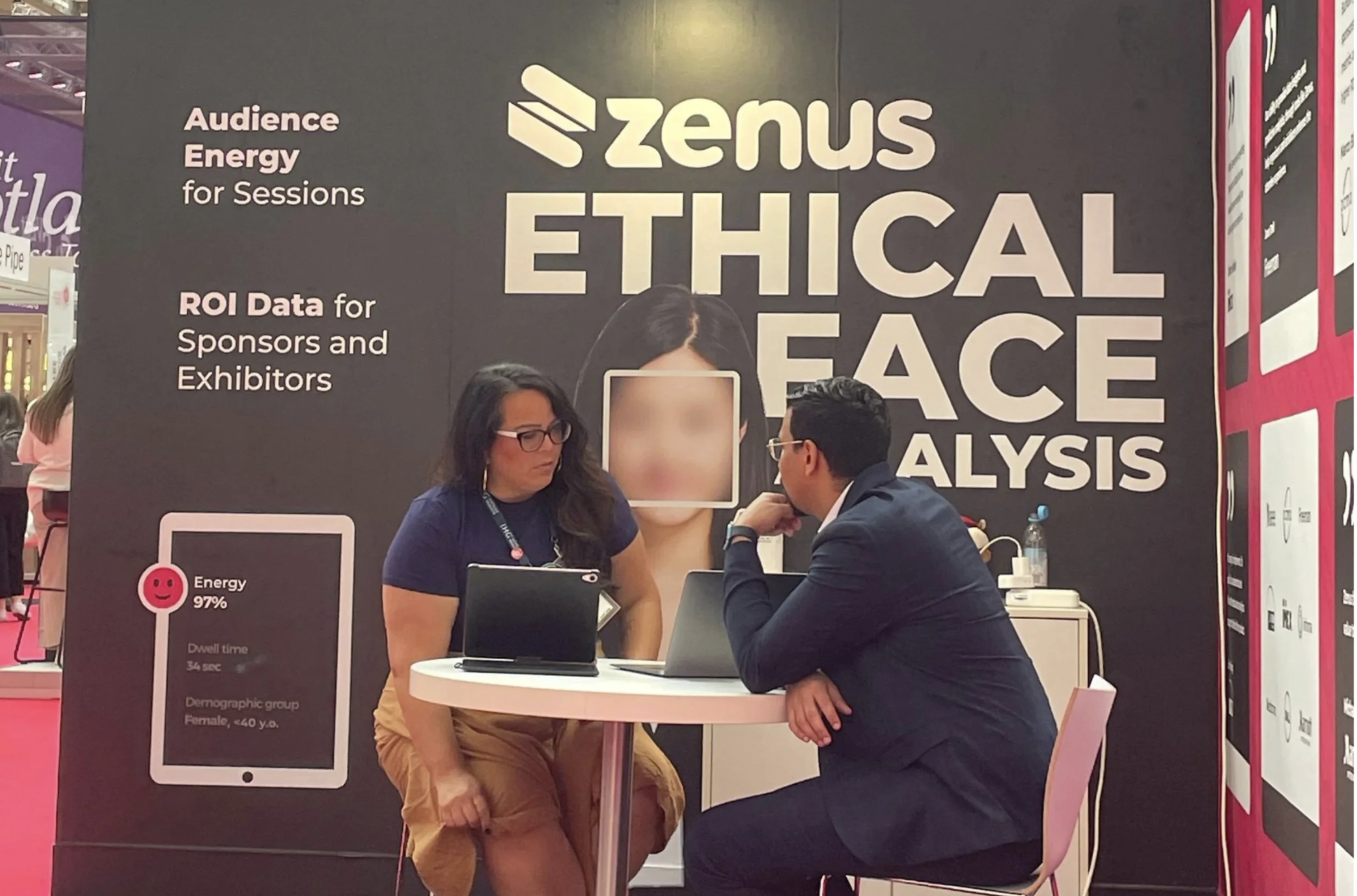 Two people seated at a table engaged in conversation at a booth with a large sign behind them reading "Zenus Ethical Face Analysis" and descriptions of audience energy and ROI data for sponsors and exhibitors.