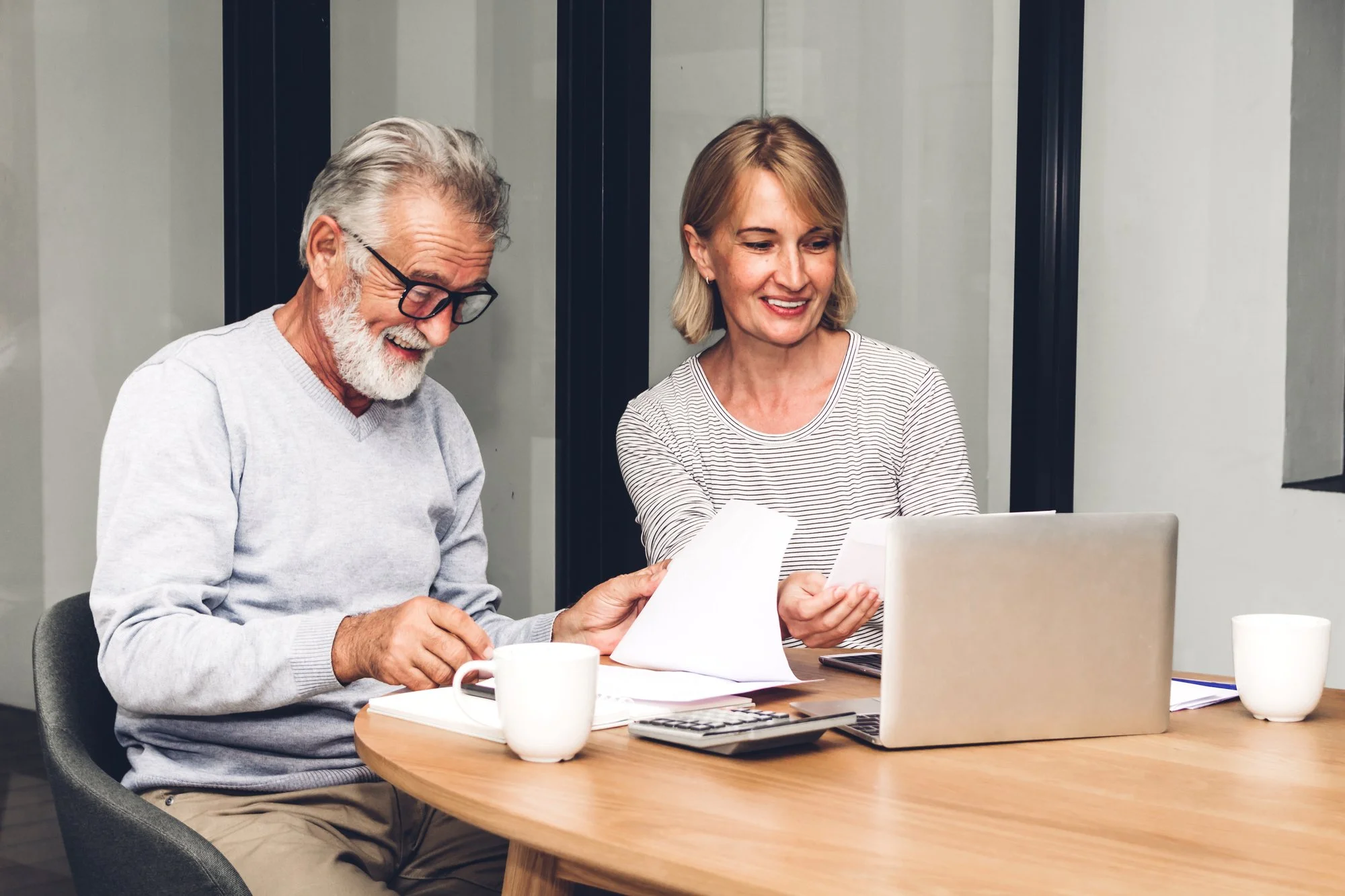 An older man and a younger woman reviewing papers together at a table with a laptop