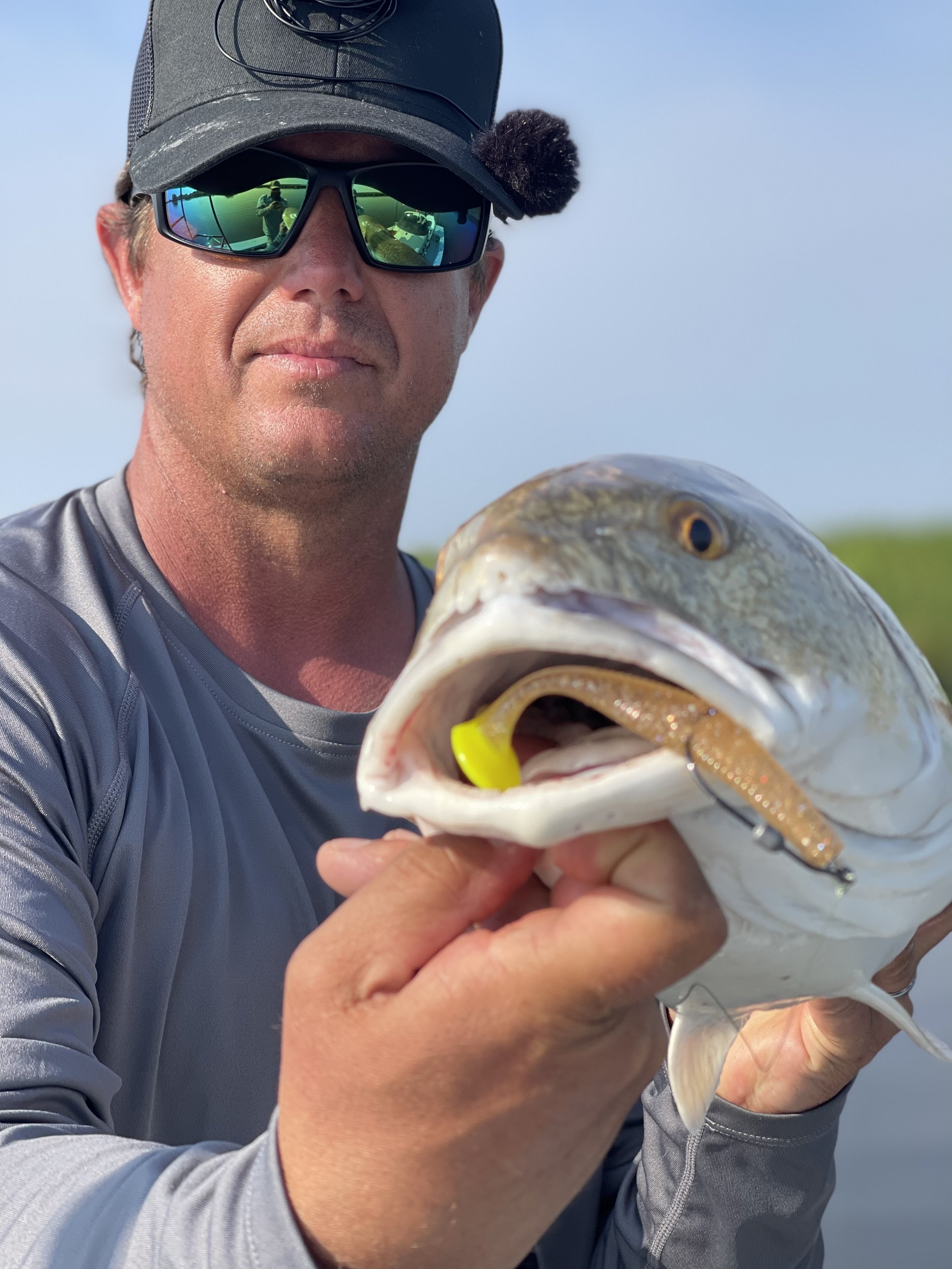 Man wearing sunglasses and a cap holding a fish with a lure in its mouth