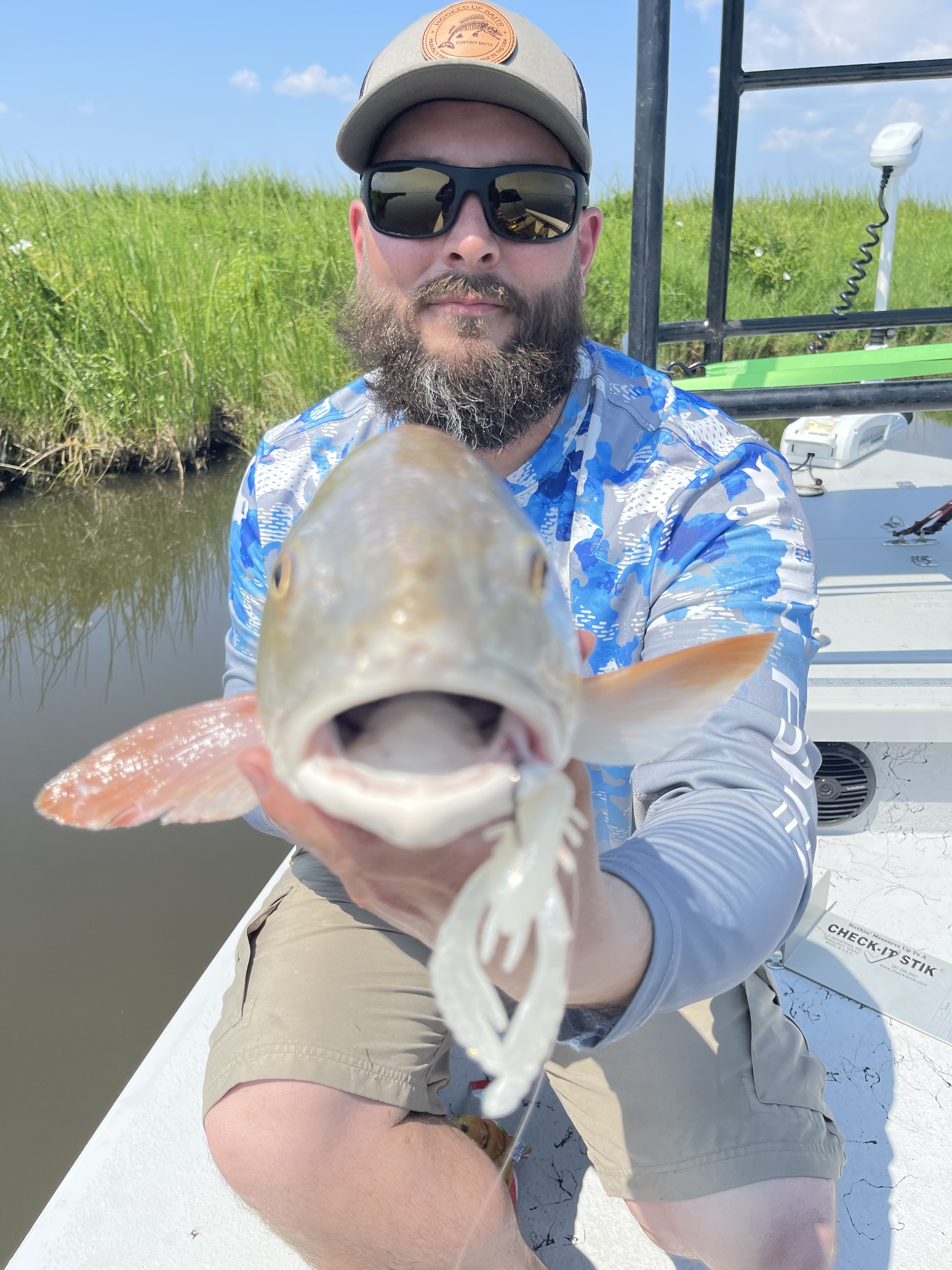 Man on a boat holding a fish with greenery in the background