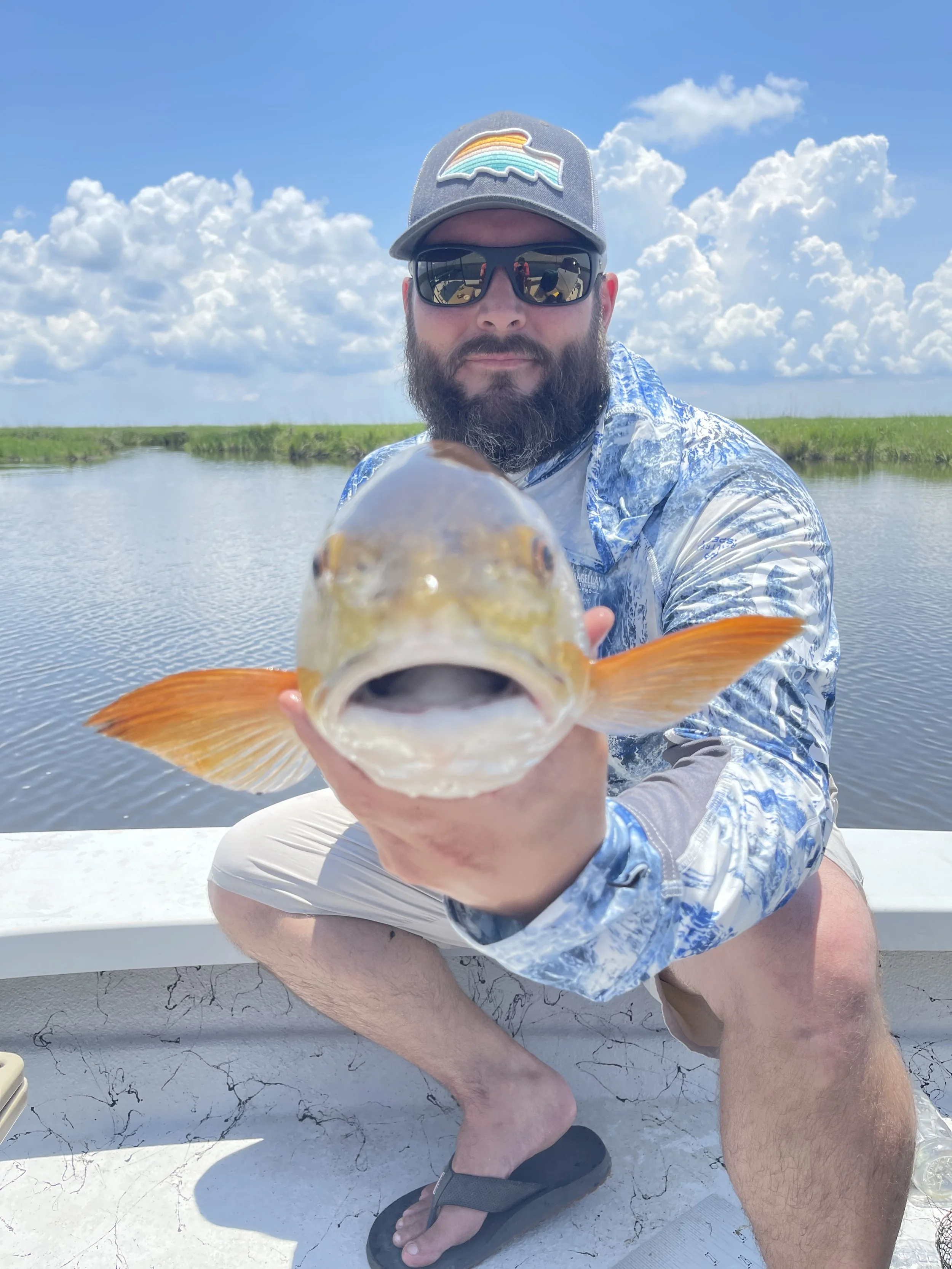 Man holding a fish on a boat with water and cloudy sky background.