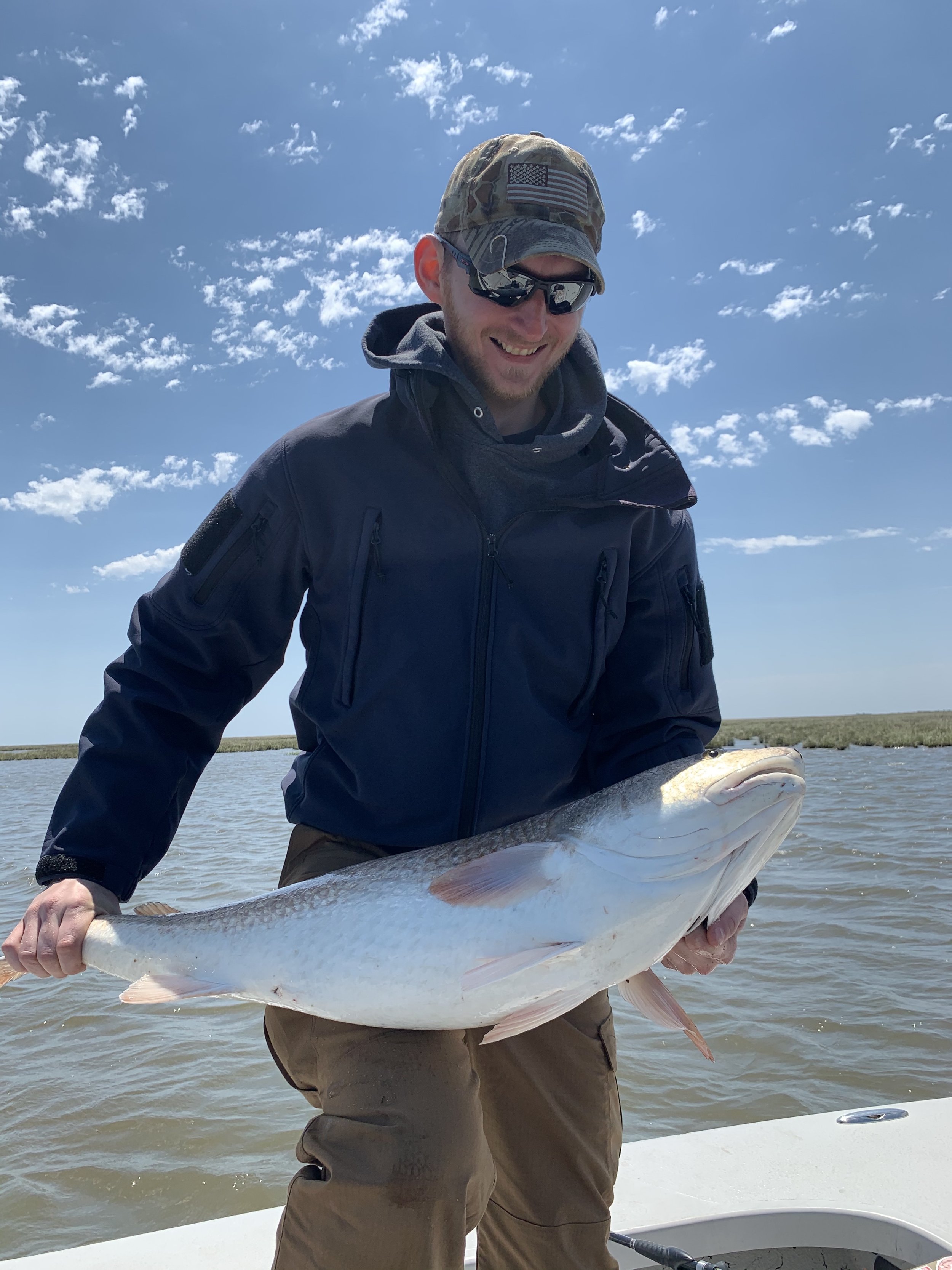 Man holding a large fish on a boat under a clear blue sky.