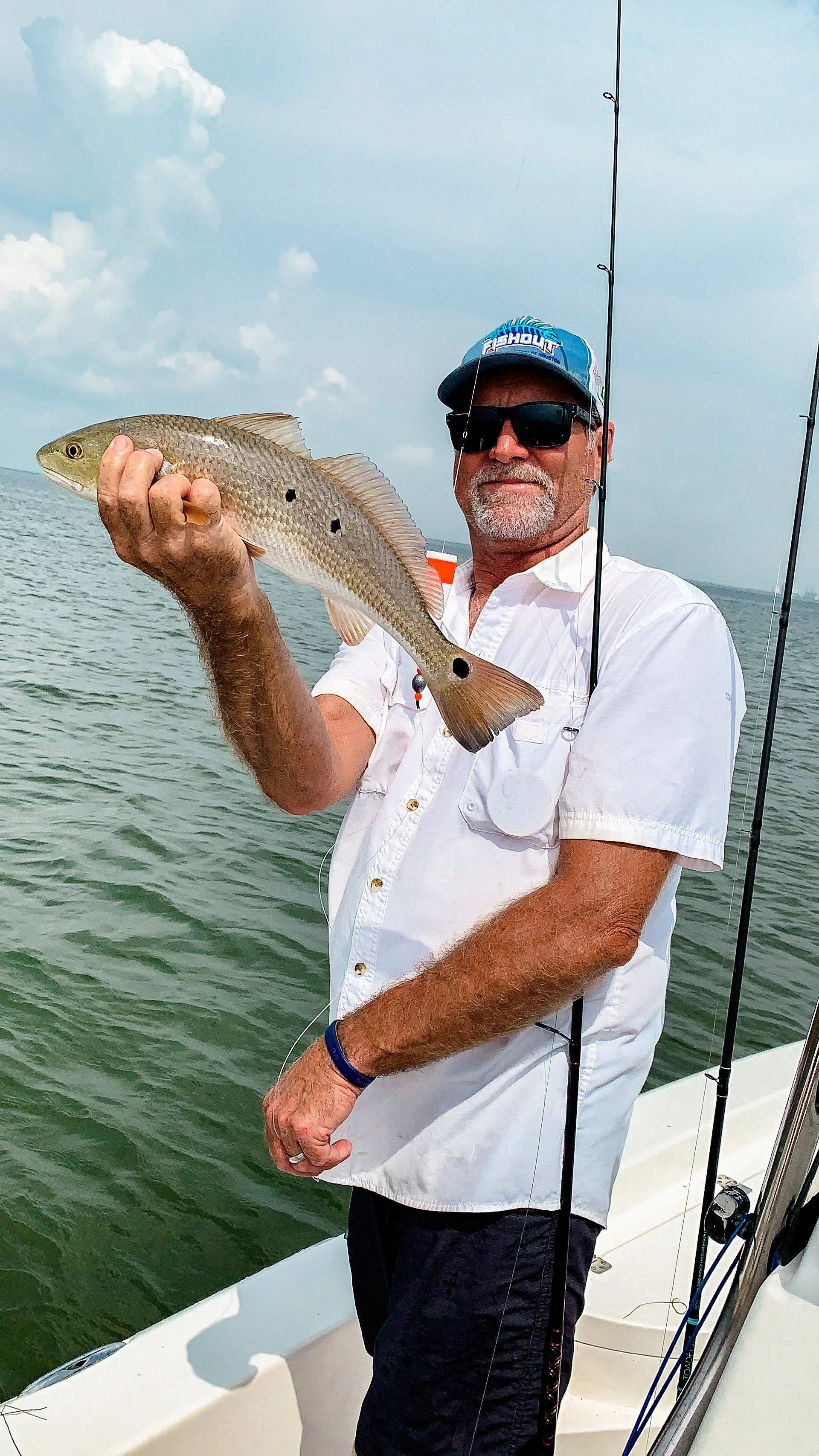 Man holding a fish on a boat with fishing rods, ocean background