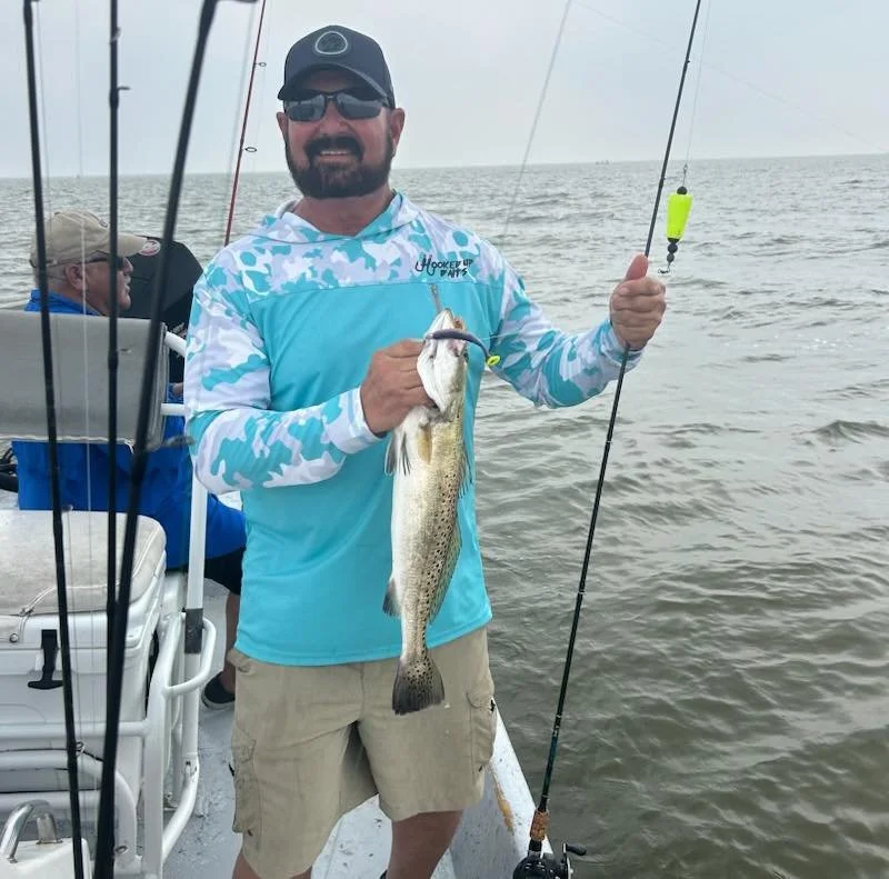 Man holding a fish standing on a boat with fishing rods in a water body.
