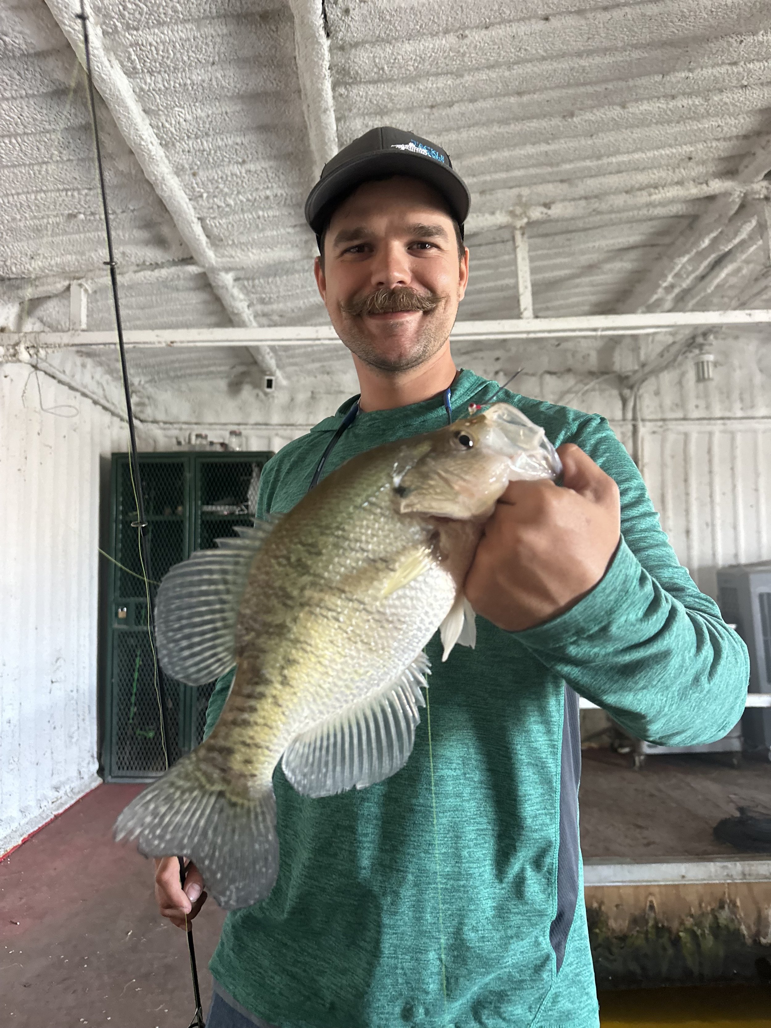 A man with a mustache and cap holding a large fish indoors.