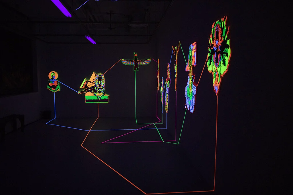 "Emanations" is an installation by artist Nafis Watson depicting deities that have been carved out using a CNC machine. The deities are painted in ultraviolet paint and connected to one another using ultraviolet tape. 